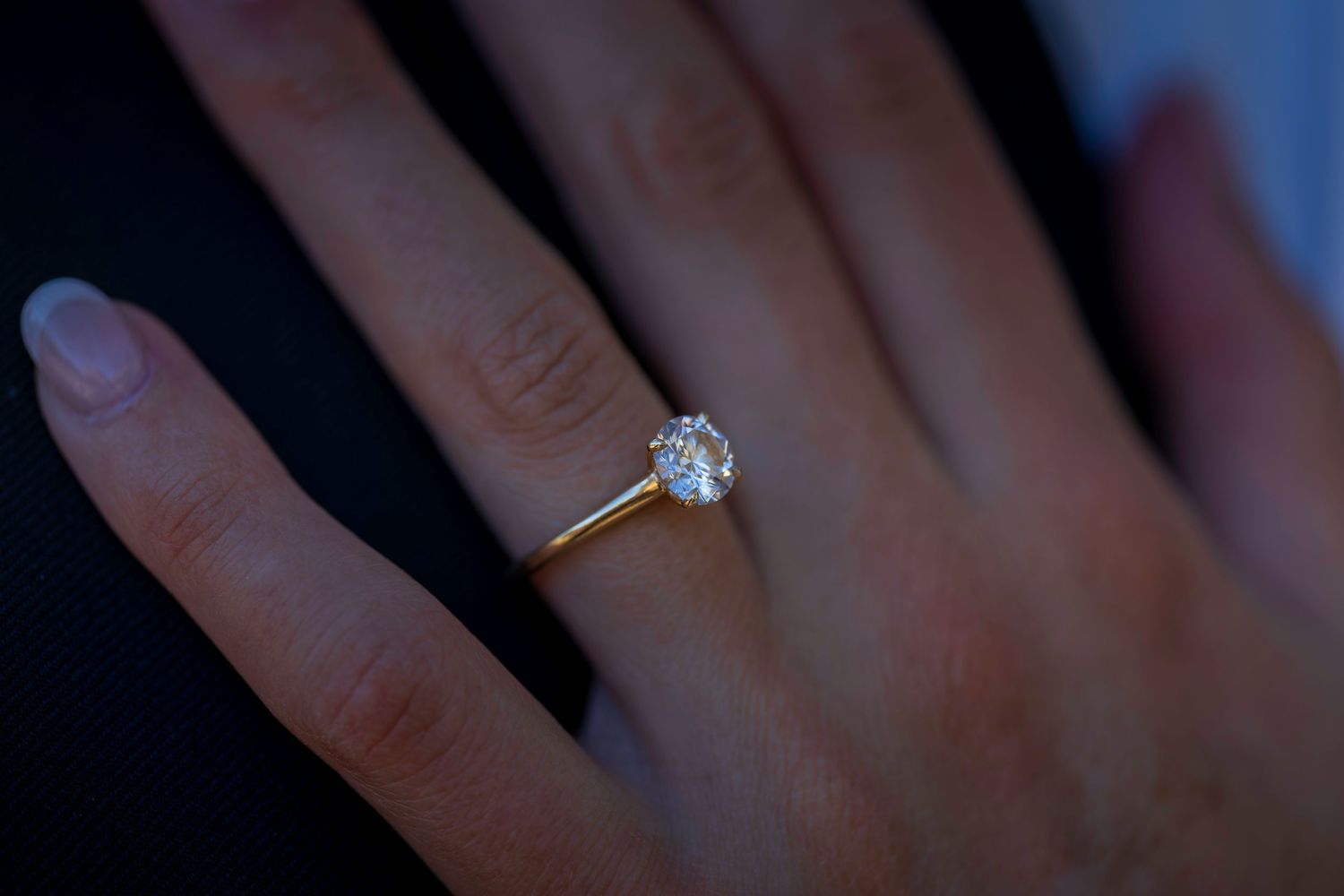 Close-up of elegant solitaire diamond engagement ring on gold band on bride's hand.