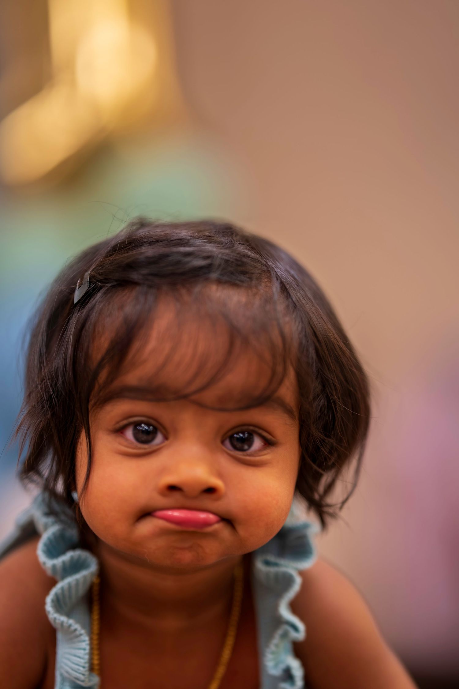 Adorable toddler girl with dark hair making a pouty face at birthday party.