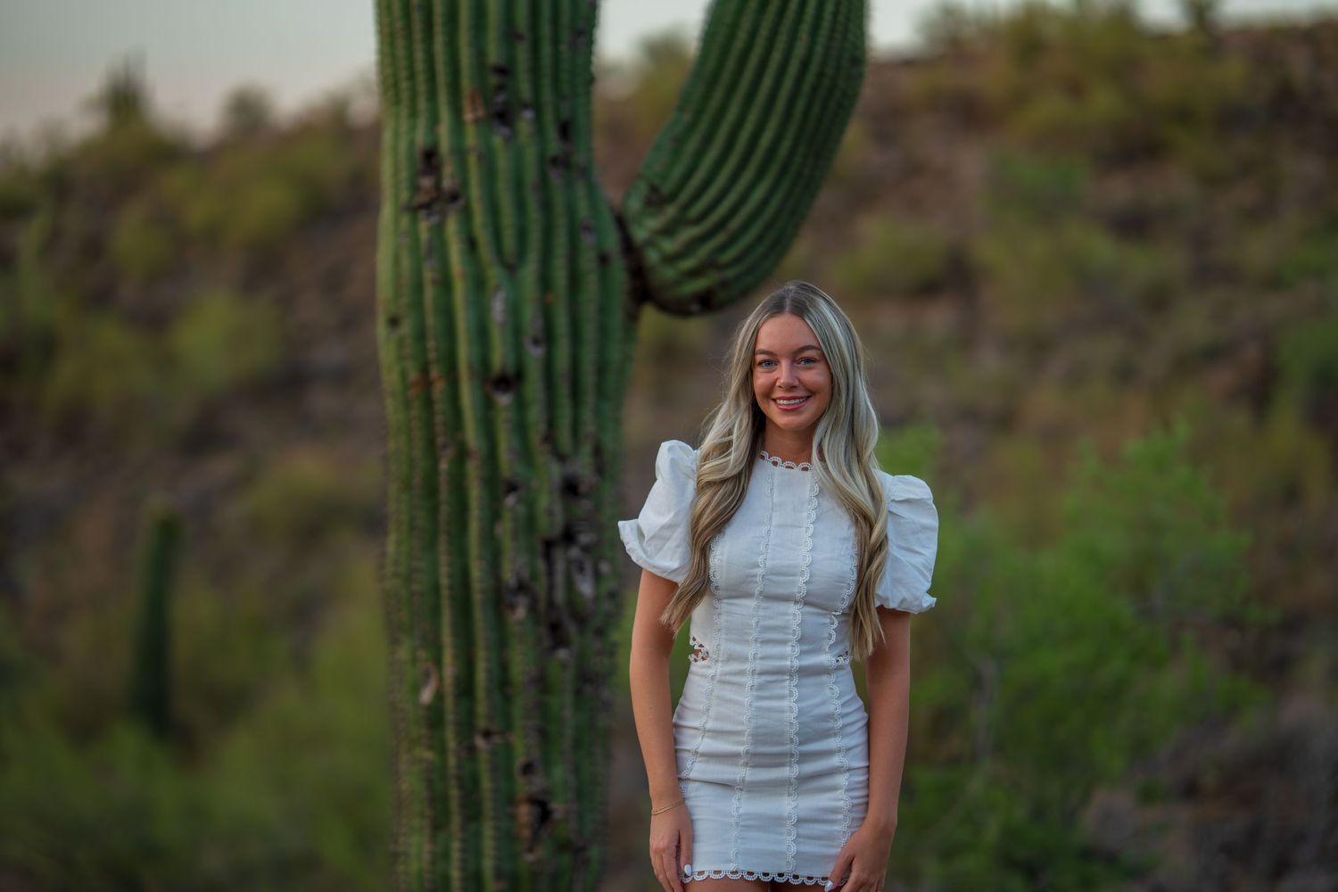 A white mini dress with puff sleeves photographed against a towering saguaro cactus in the desert at sunset.