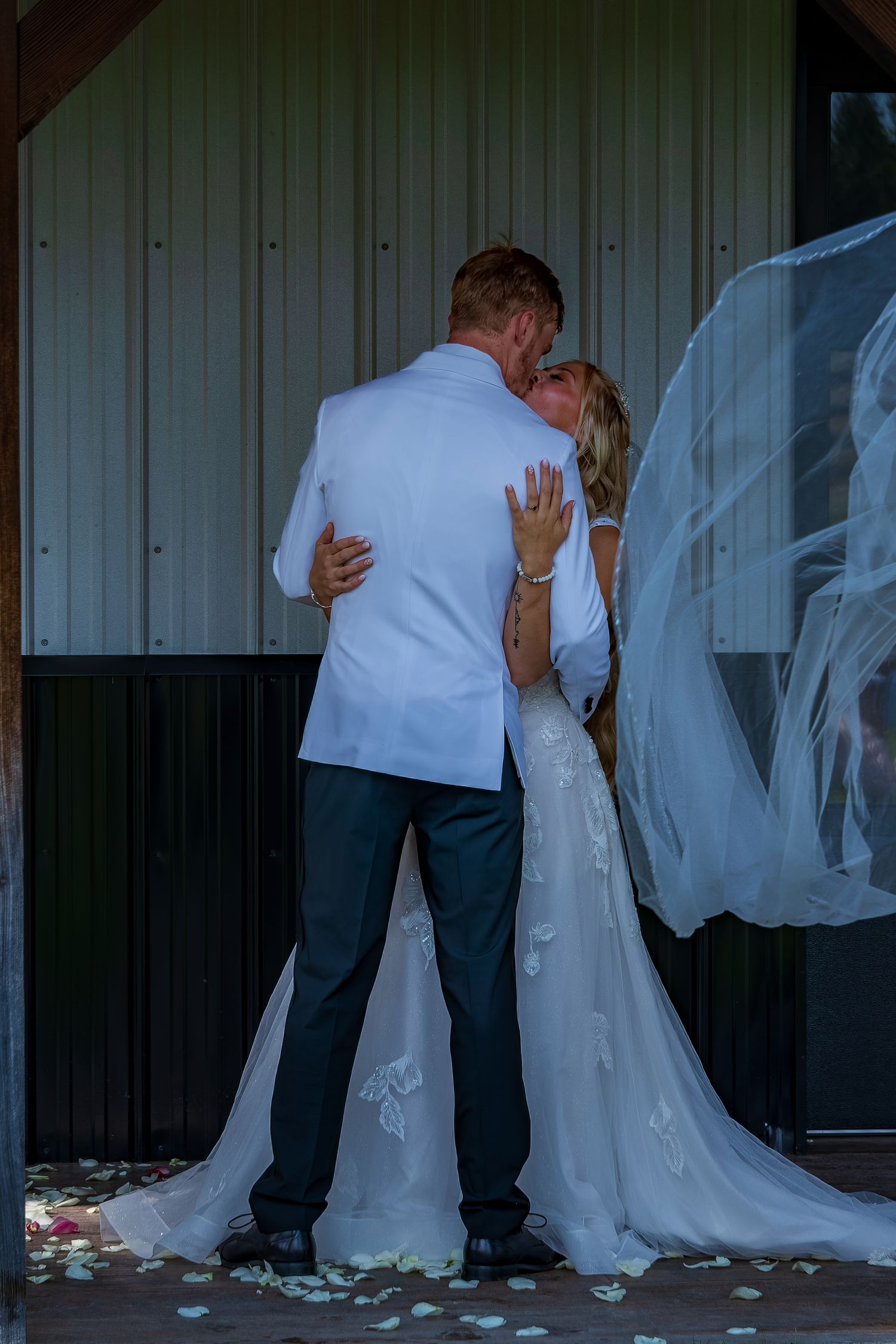 Wedding couple shares intimate poses and embraces in front of a metal wall with scattered petals.