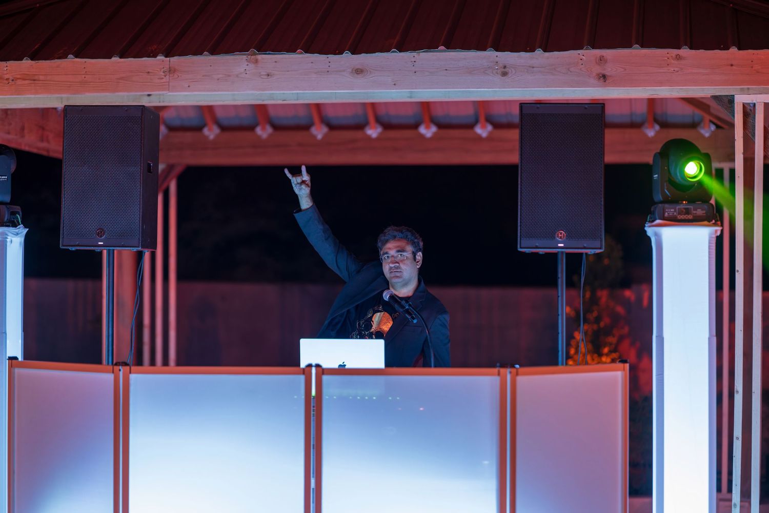 DJ performs from elevated booth with raised hand at nighttime event.