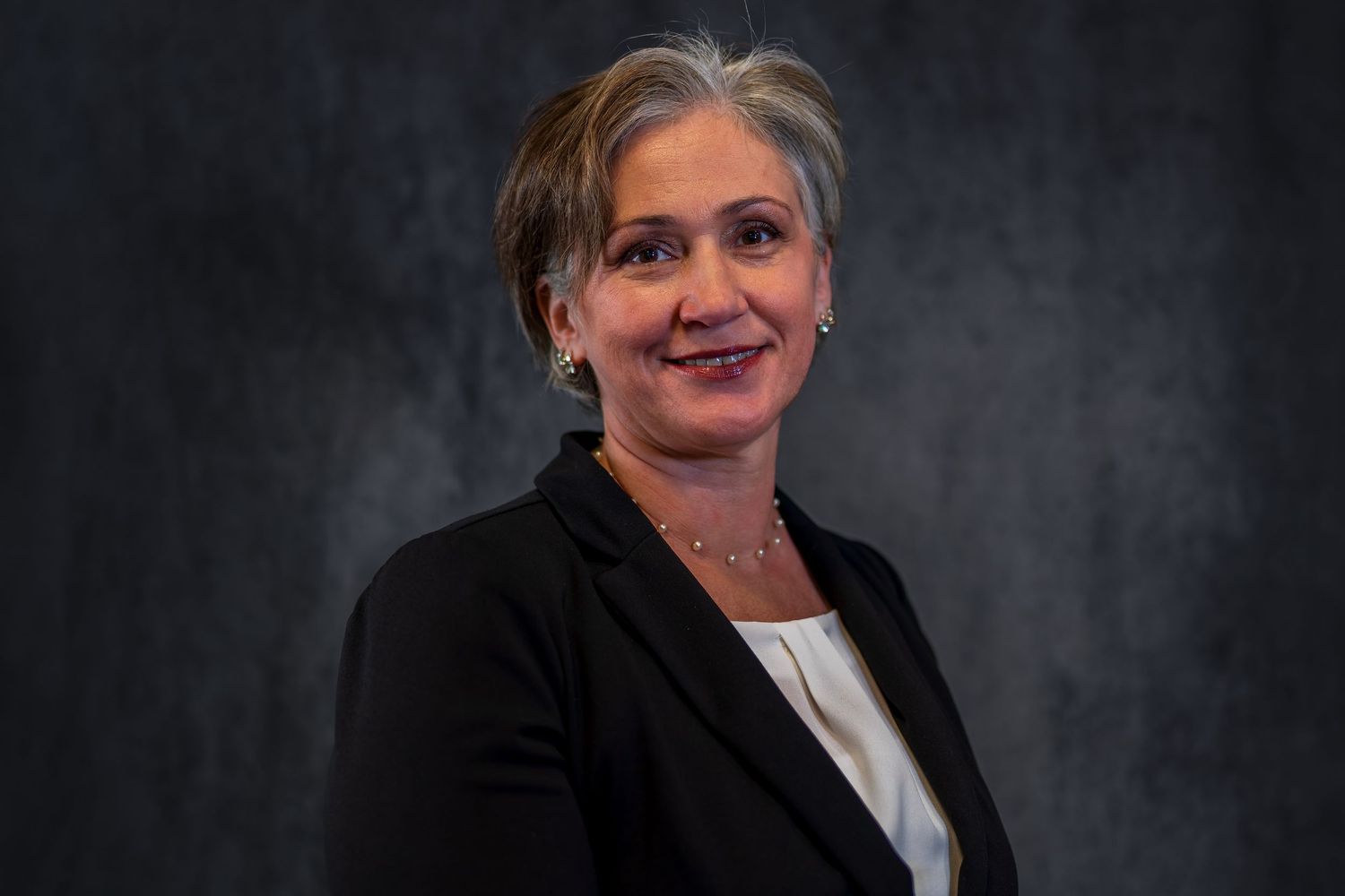 Professional headshot with warm expression against dark studio background.