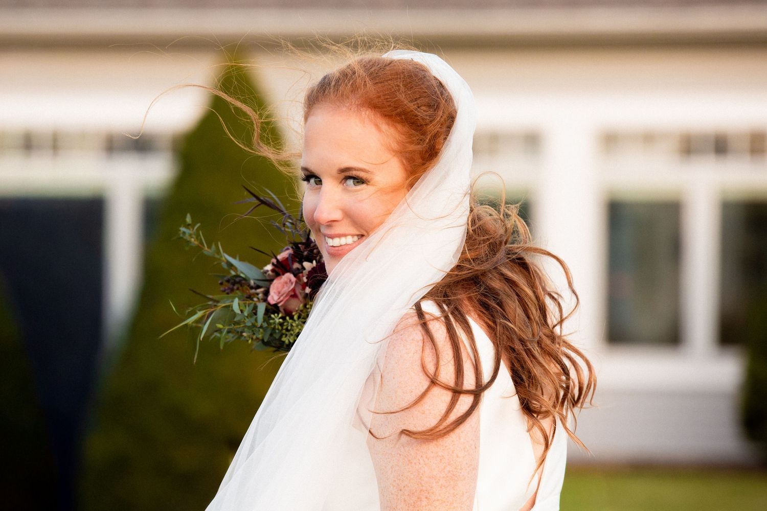 Radiant red-haired bride with flowing veil and bouquet smiling outdoors on wedding day, Xenia Helix Photography, Boston, MA