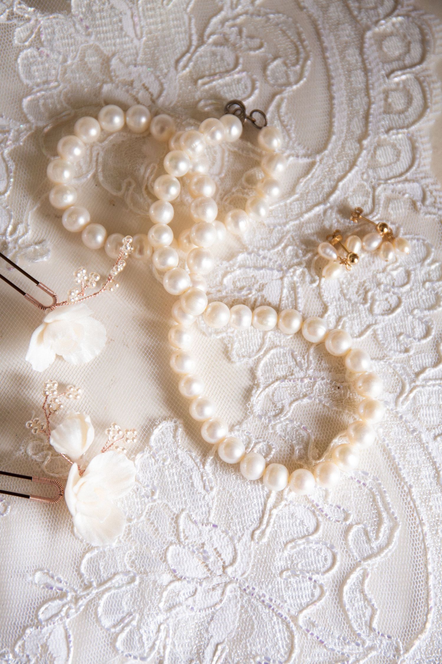 Pearl bracelets and floral porcelain hairpins arranged on white lace wedding fabric, The Endicott Estate, Dedham, MA