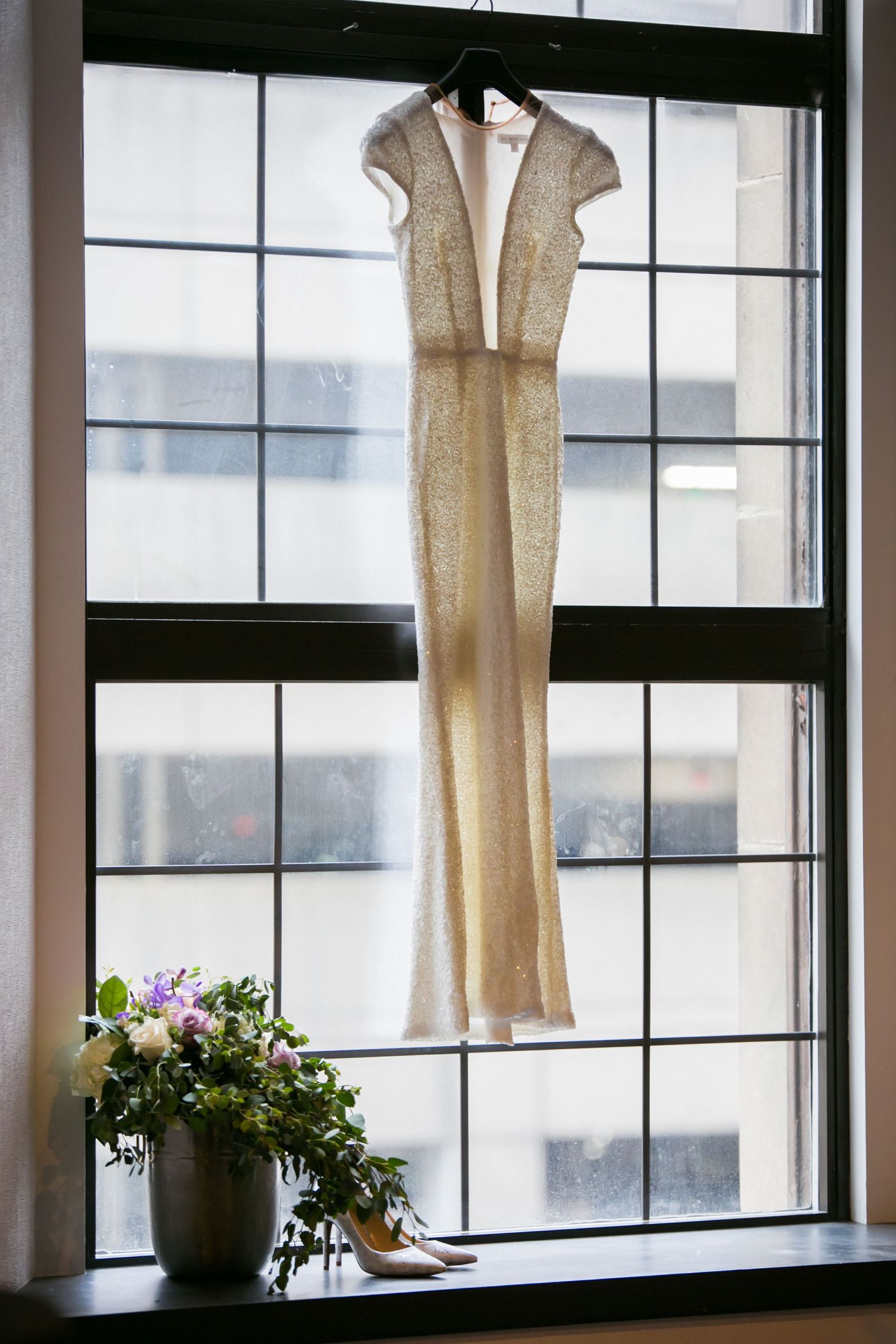 Elegant sleeveless wedding gown hangs in window above bridal heels and floral bouquet, Courtyard by Marriott Boston Downtown, Boston, MA