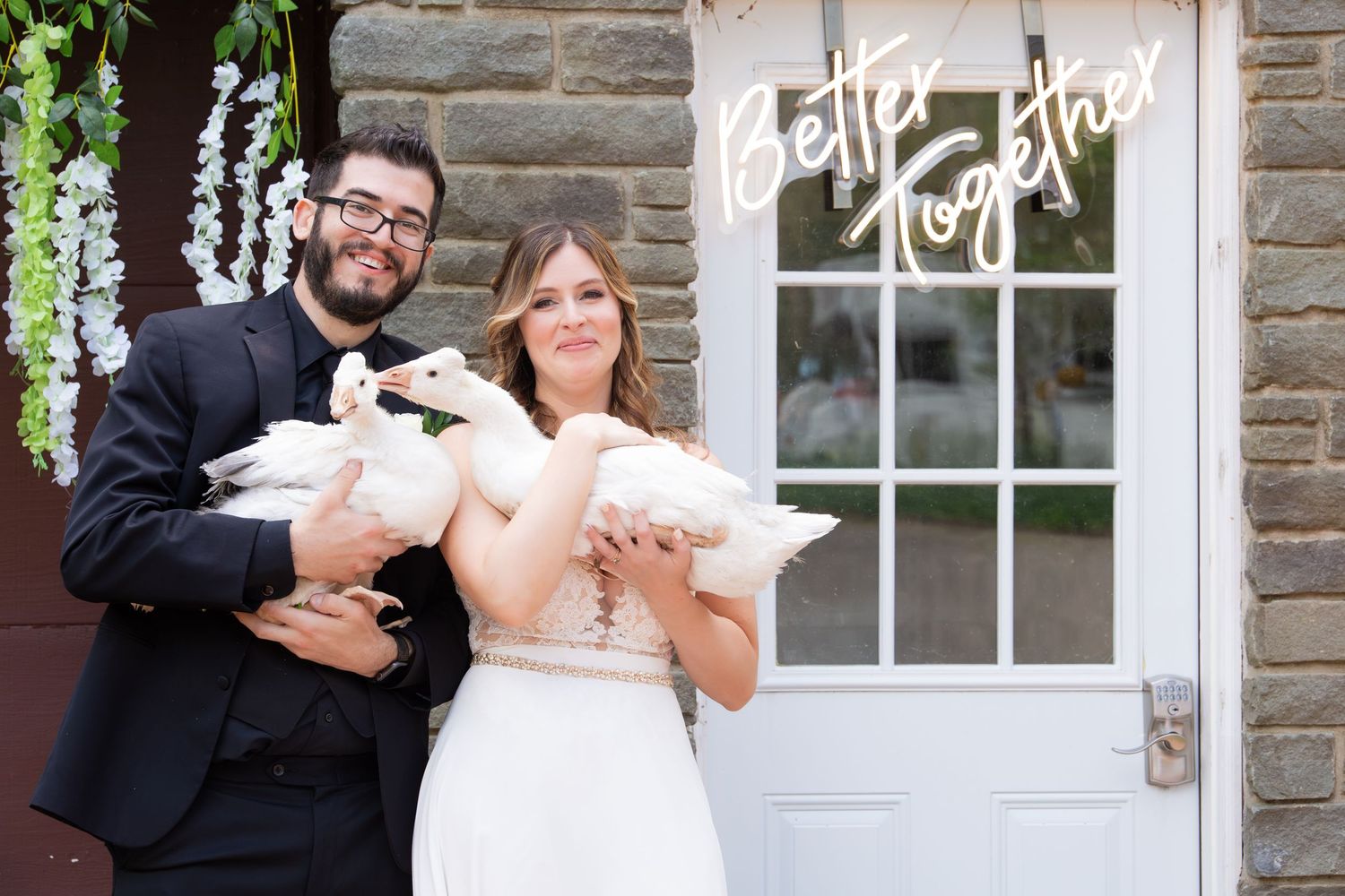 Smiling couple holding white geese in front of a Better Together sign at their wedding, Xenia Helix Photography, Boston, MA