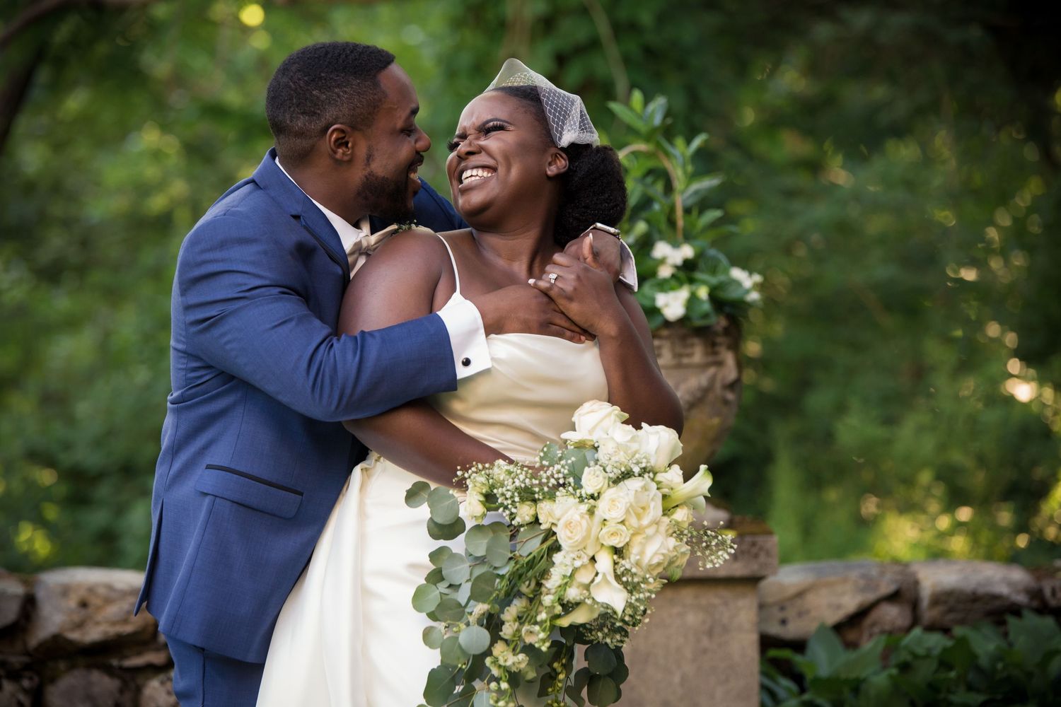 Joyful couple embracing outdoors on their wedding day, bride holding white bouquet, groom in blue suit, The Connors Center, Dover, MA