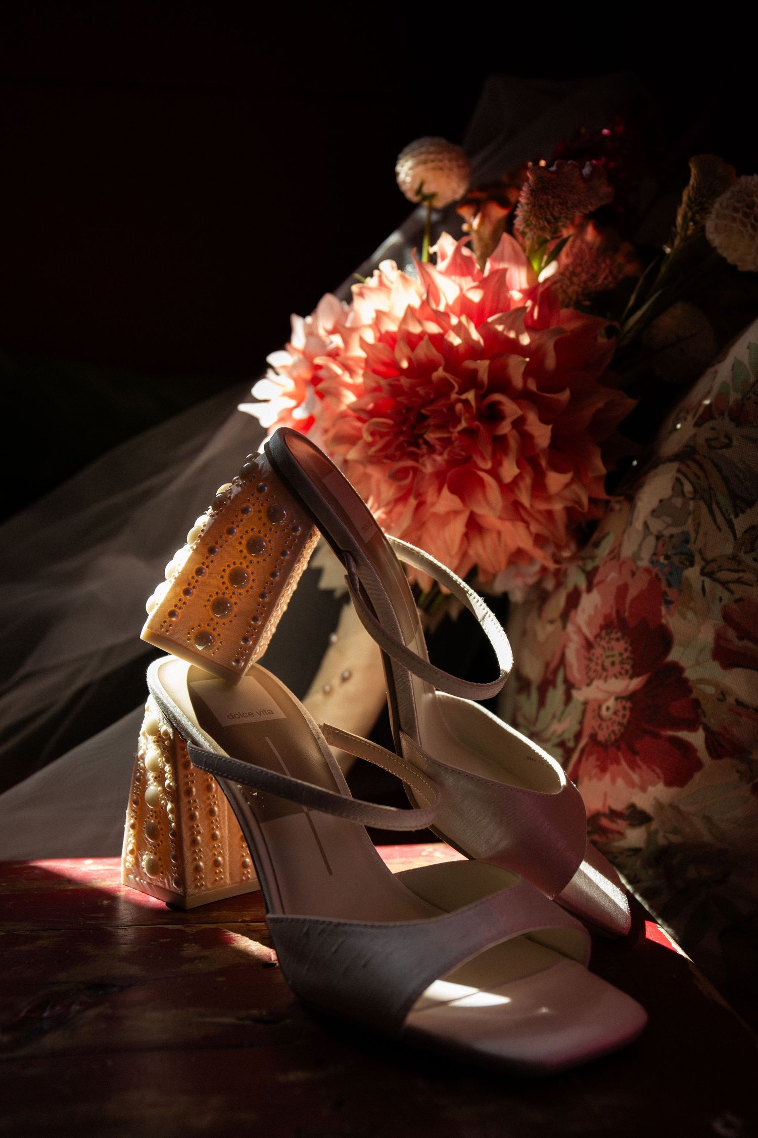 Elegant white bridal heels with pearl studded block heels beside pink dahlia bouquet in dark setting, 	The Red Lion Inn, Cohasset, MA