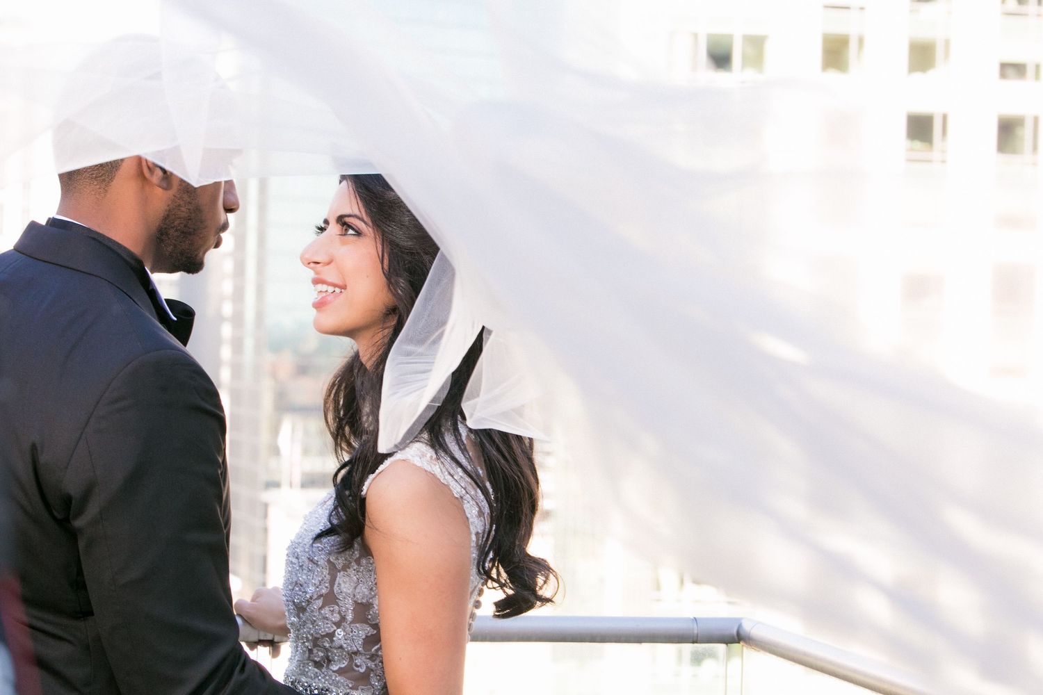 Bride in lace gown with billowing veil and groom in black tuxedo share a romantic rooftop moment, Mandarin Oriental Boston, Boston, MA