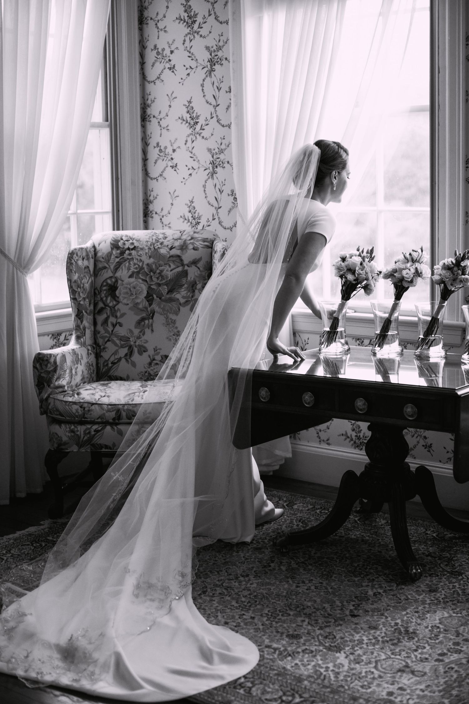 Elegant bride in cathedral veil looking out of the window in black and white portrait, Lyman Estate, Waltham, MA