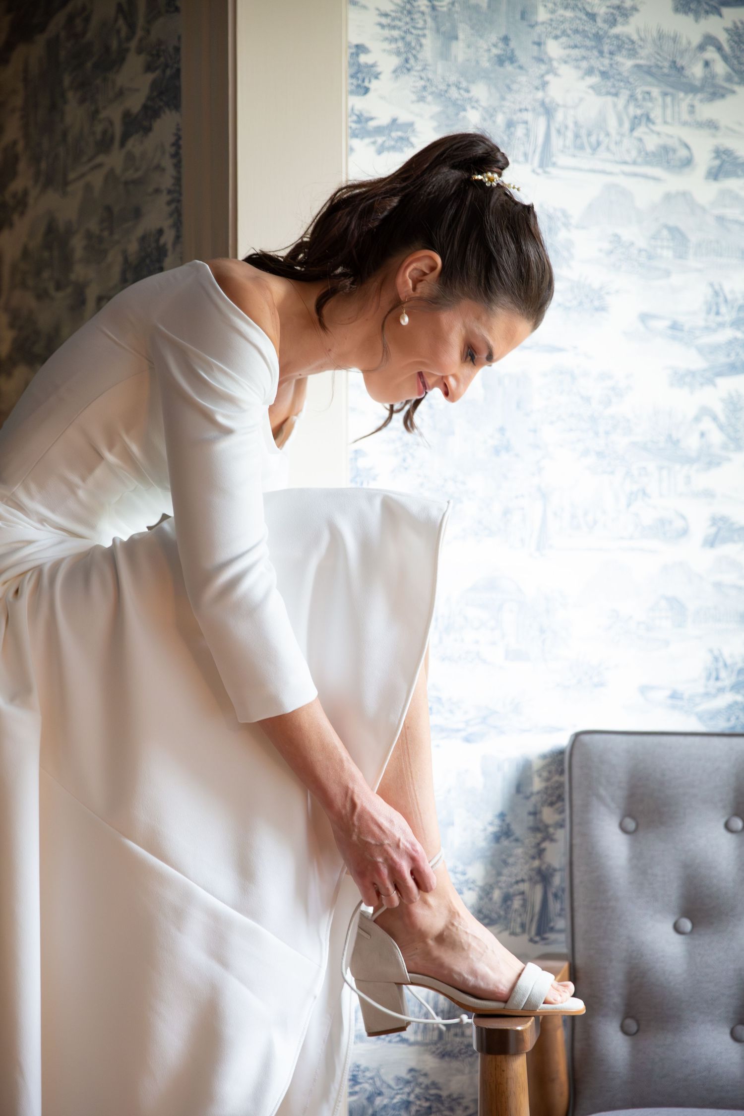 Bride in a minimalistic gown, putting on elegant dusty-blue heeled wedding shoes, Xenia Helix Photography, Boston, MA