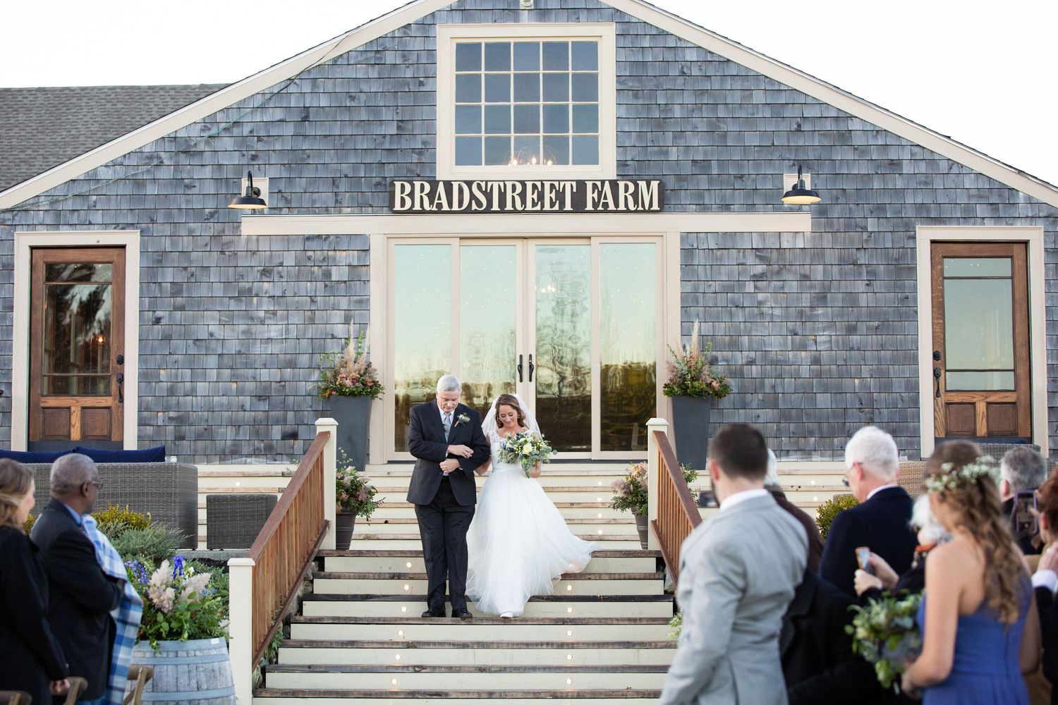 The bride walks down the outdoor steps with her father at the wedding ceremony, Barn at Bradstreet Farm, Rowley, MA