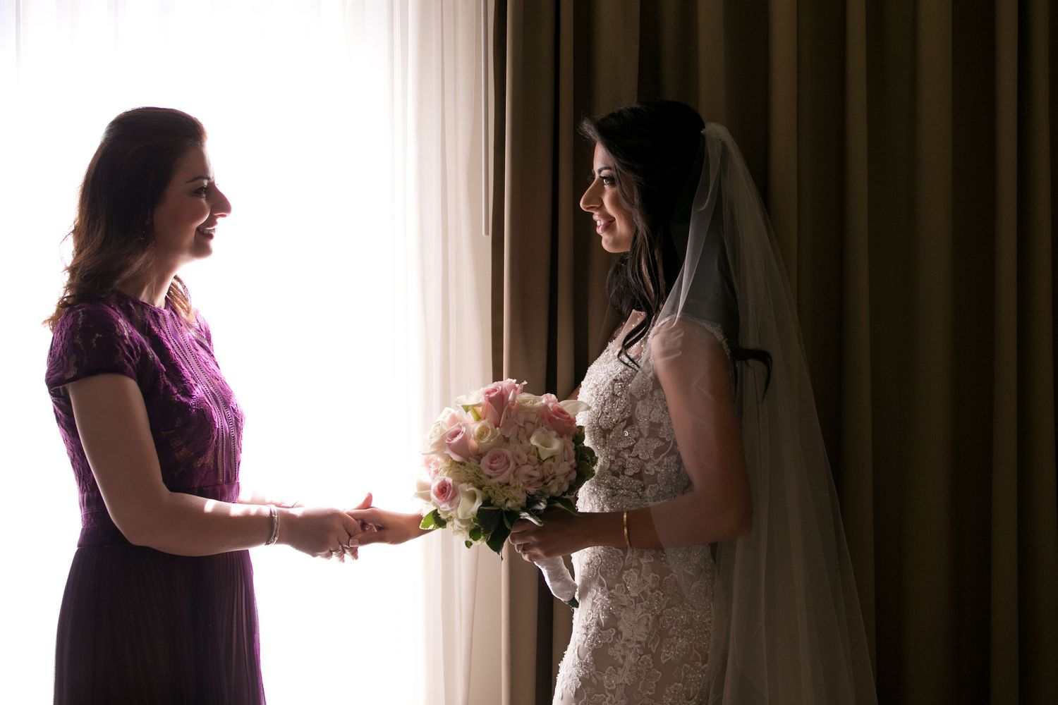 Smiling mother presents a pink bouquet to the bride in a lace gown near a sunlit window, Mandarin Oriental Boston, Boston, MA