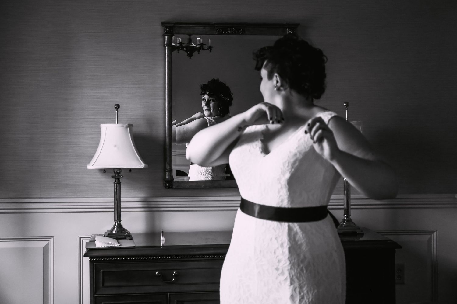 Black and white photo of a bride adjusting her dress in front of a vintage mirror, Inn on Boltwood, Amherst, MA