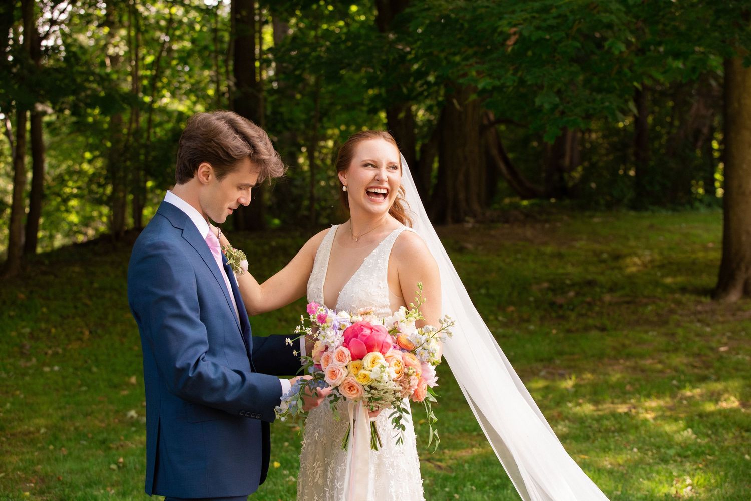 A laughing bride in a lace gown holds colorful blooms while sharing a joyful moment with her groom, Grove at Briar Barn Inn, Rowley, MA