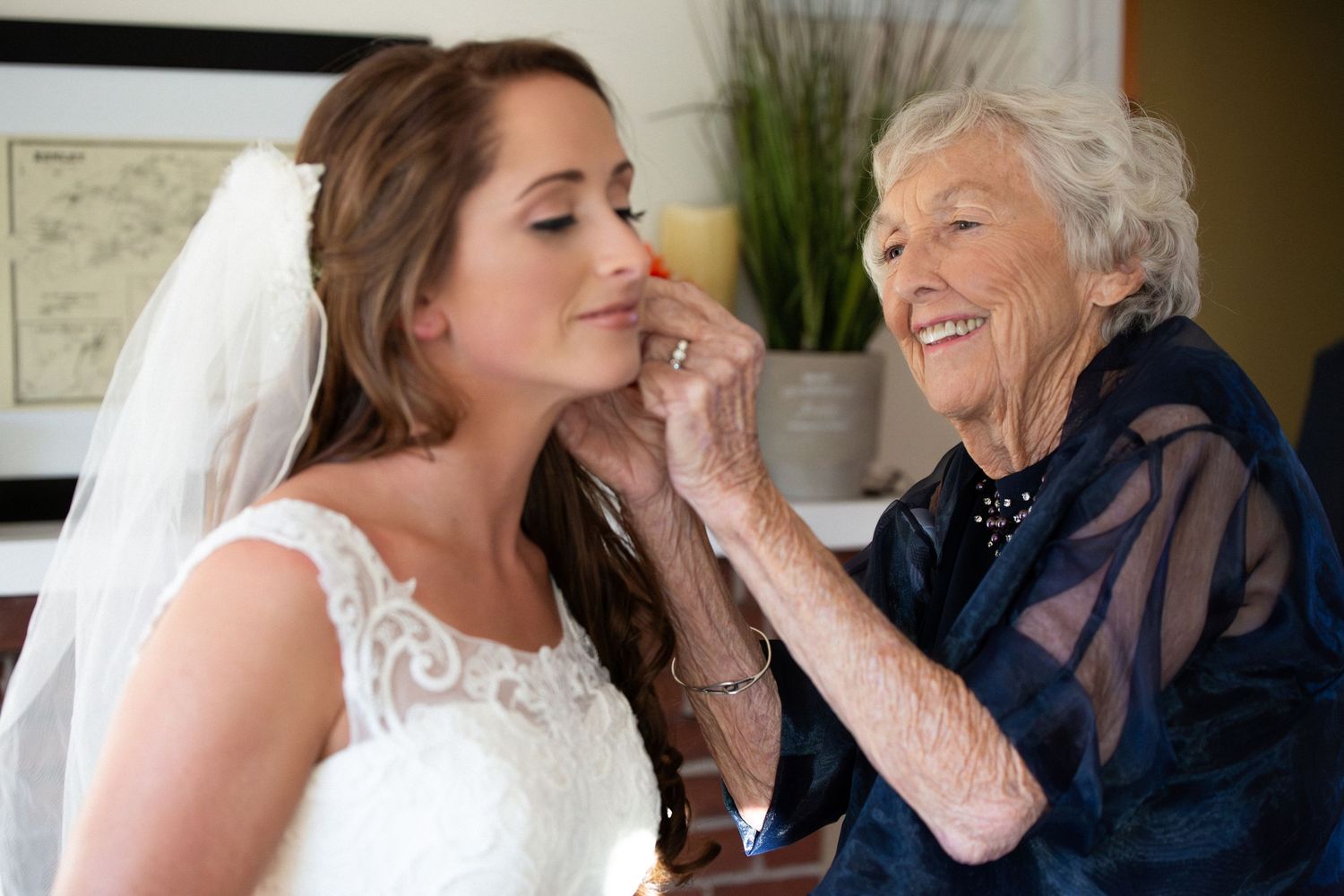 Elderly grandmother smiling while putting an earring on a bride in a white lace wedding dress, Barn at Bradstreet Farm, Rowley, MA