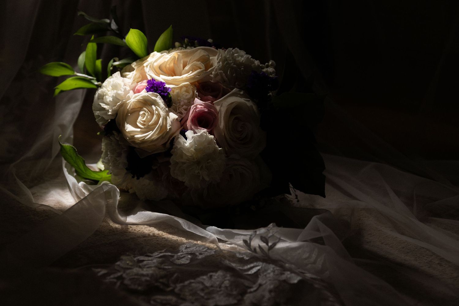 Round wedding bouquet of white and pink roses resting on delicate lace veil in soft dramatic lighting, Estate at Moraine Farm, Beverly, MA
