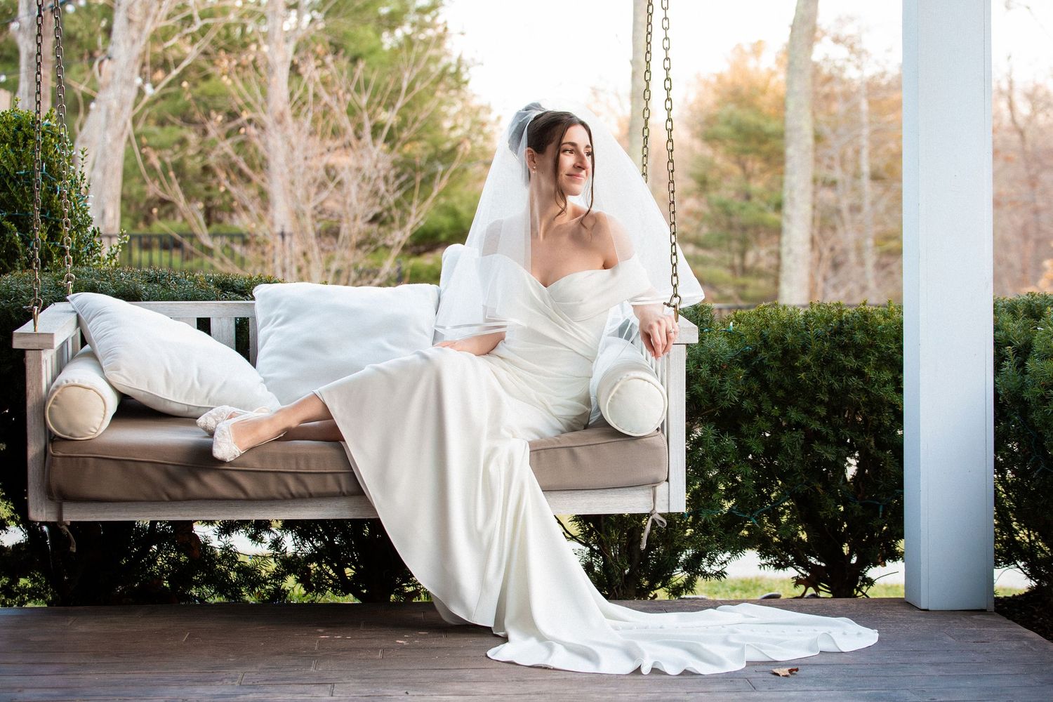 Serene bride in strapless white gown and veil sits gracefully on an outdoor porch swing, Grove at Briar Barn Inn, Rowley, MA