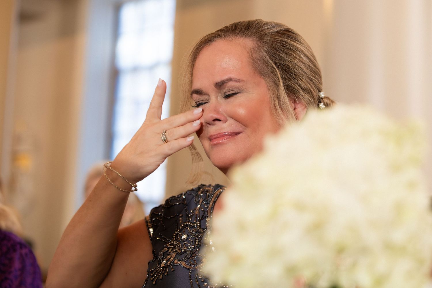 Emotionalmom of the bride wipes tears during touching ceremony moment with white floral arrangement, Xenia Helix Photography, Boston, MA