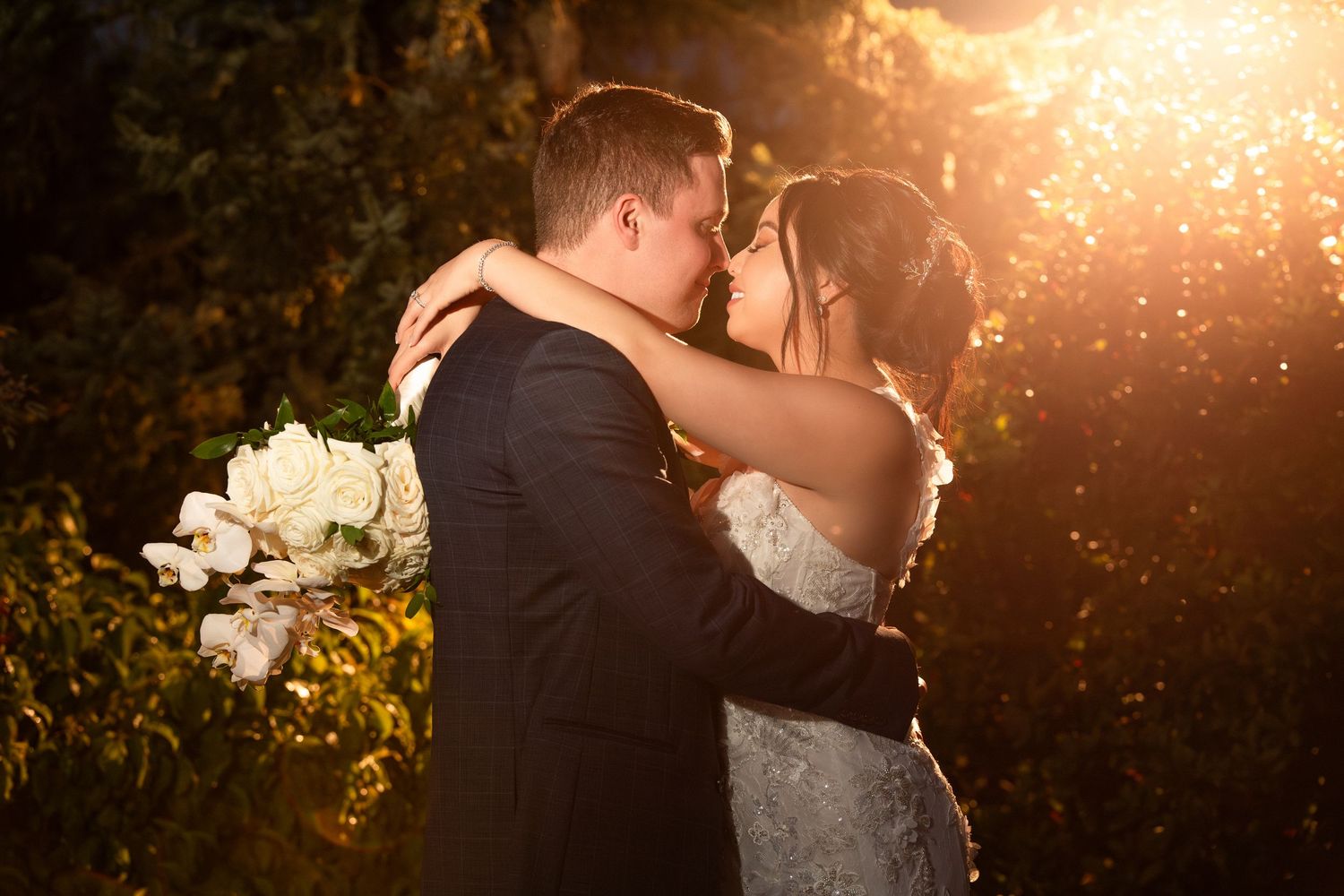 Bride and groom kiss outdoors in golden sunset light, bride holding white orchids, Harrington Farm, Princeton, MA