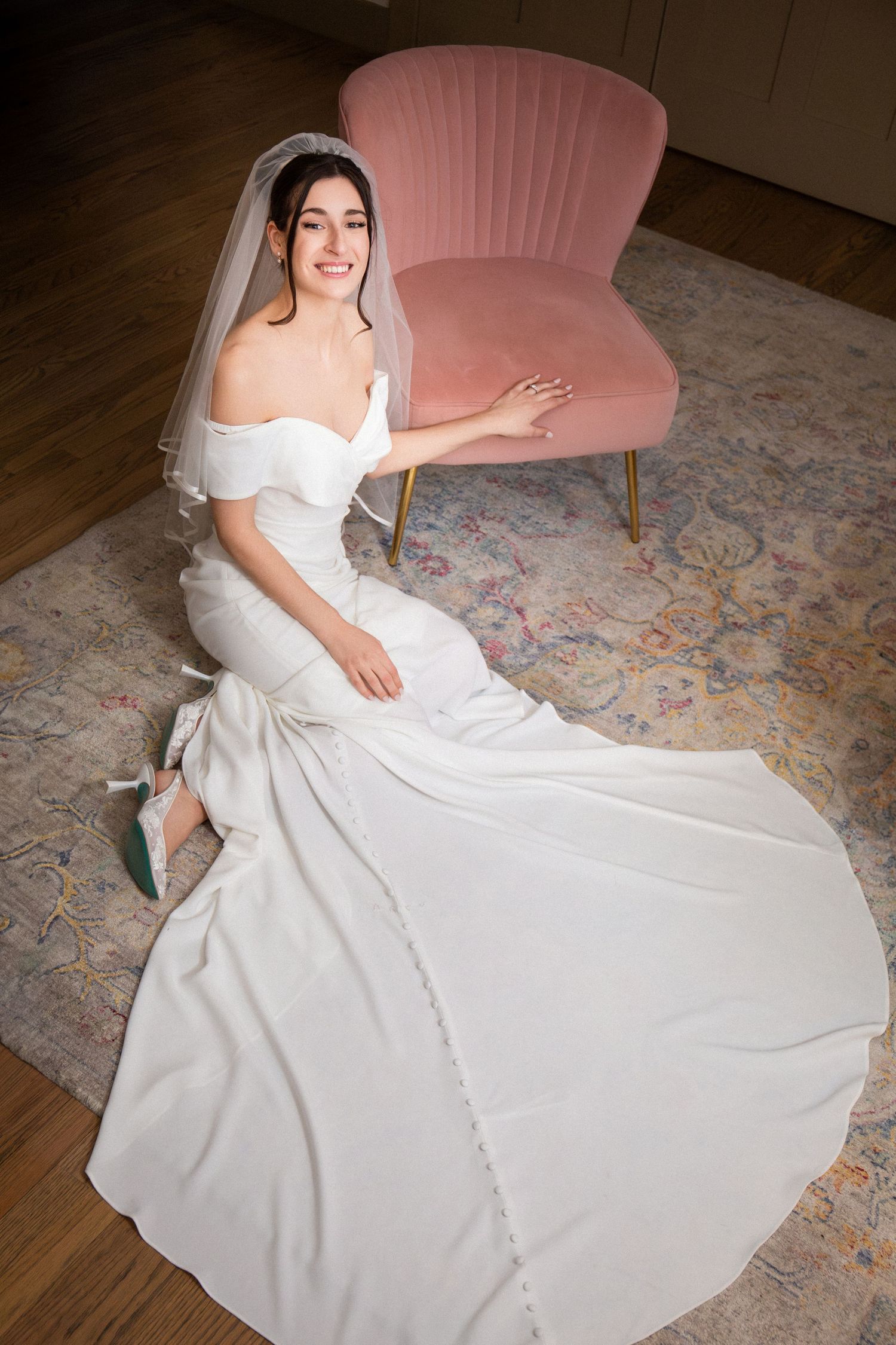 Elegant bride in off-shoulder white gown seated on floor beside pink velvet chair, Grove at Briar Barn Inn, Rowley, MA