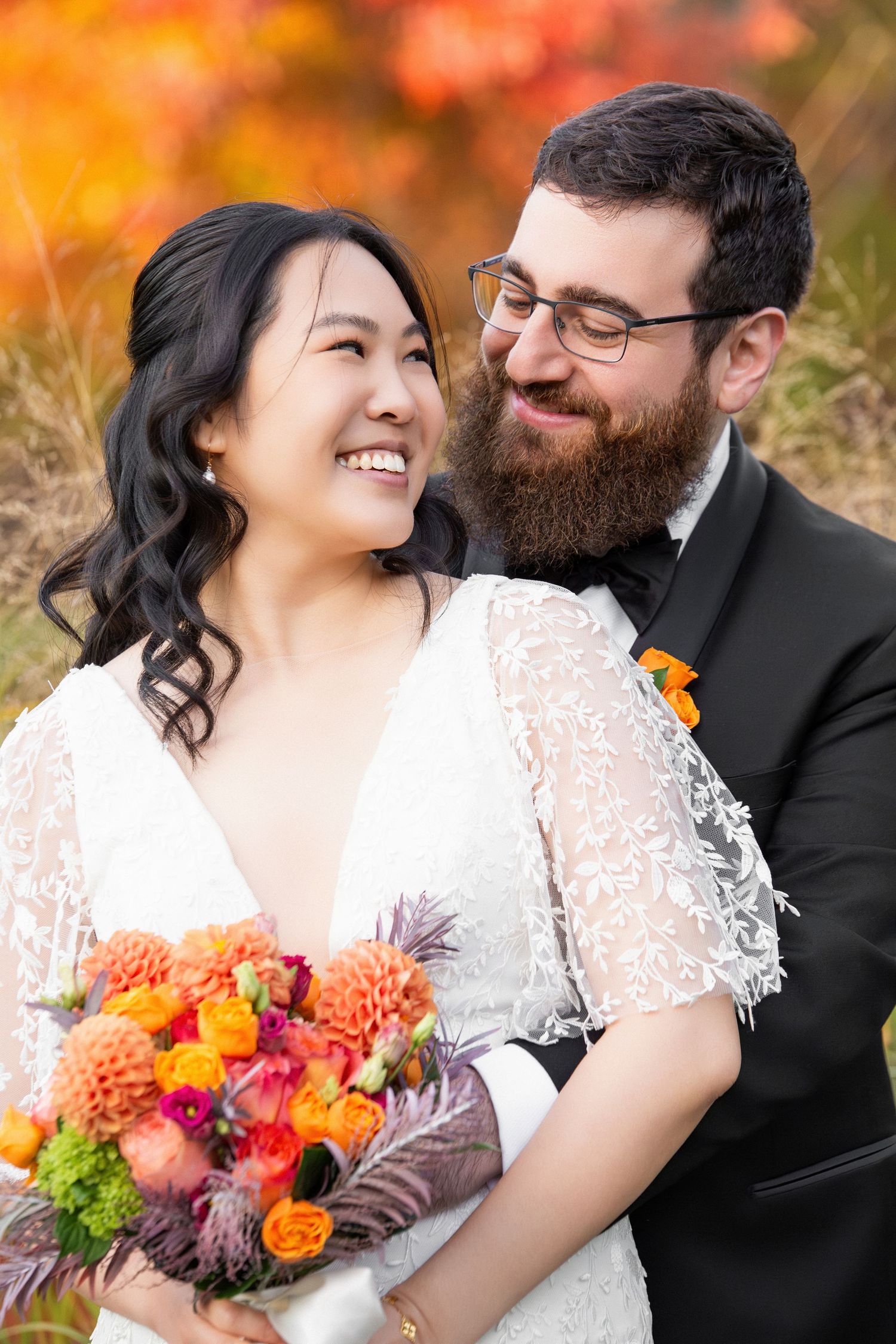 Smiling bride and bearded groom embracing amid autumn foliage with a colorful bouquet, Alewife Brook Reservation, Cambridge, MA