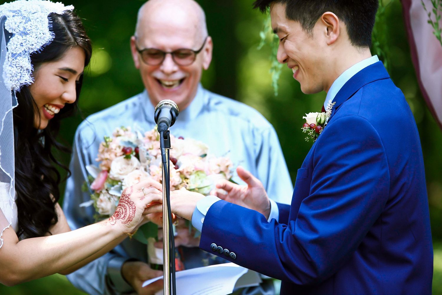 Bride and groom exchange rings during outdoor wedding ceremony with officiant at microphone, Mass Audubon's Habitat, Belmont, MA