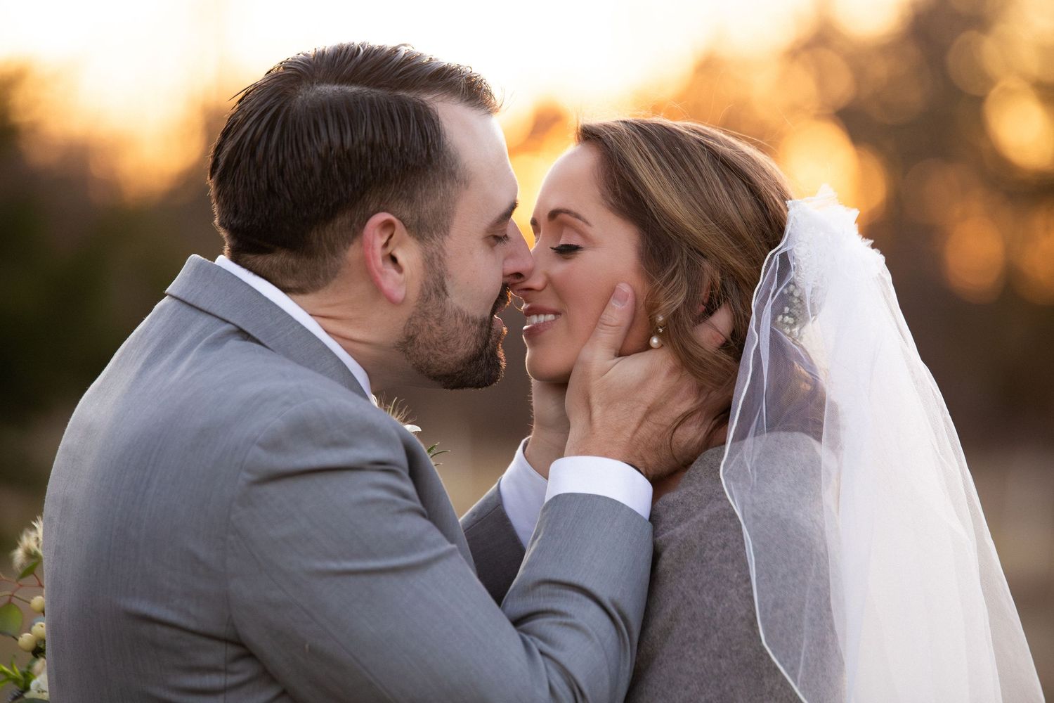 Groom in gray suit tenderly kisses smiling bride at golden sunset, Barn at Bradstreet Farm, Rowley, MA