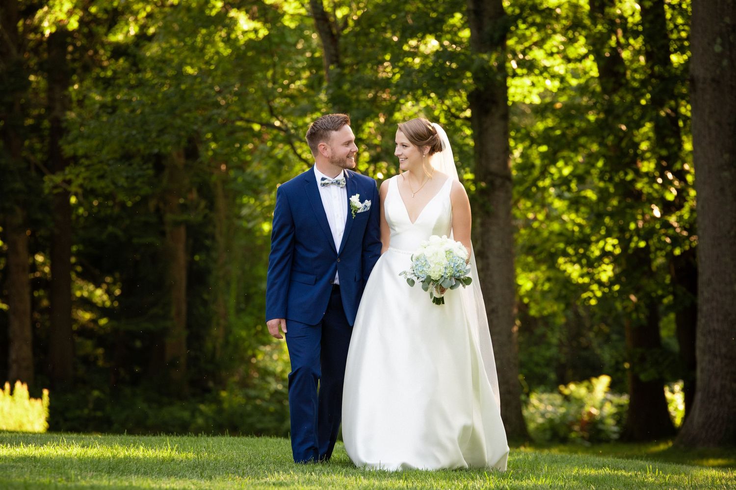 Bride and groom walking hand in hand through lush green trees on their wedding day, Stevens Estate at Osgood Hill, North Andover, MA