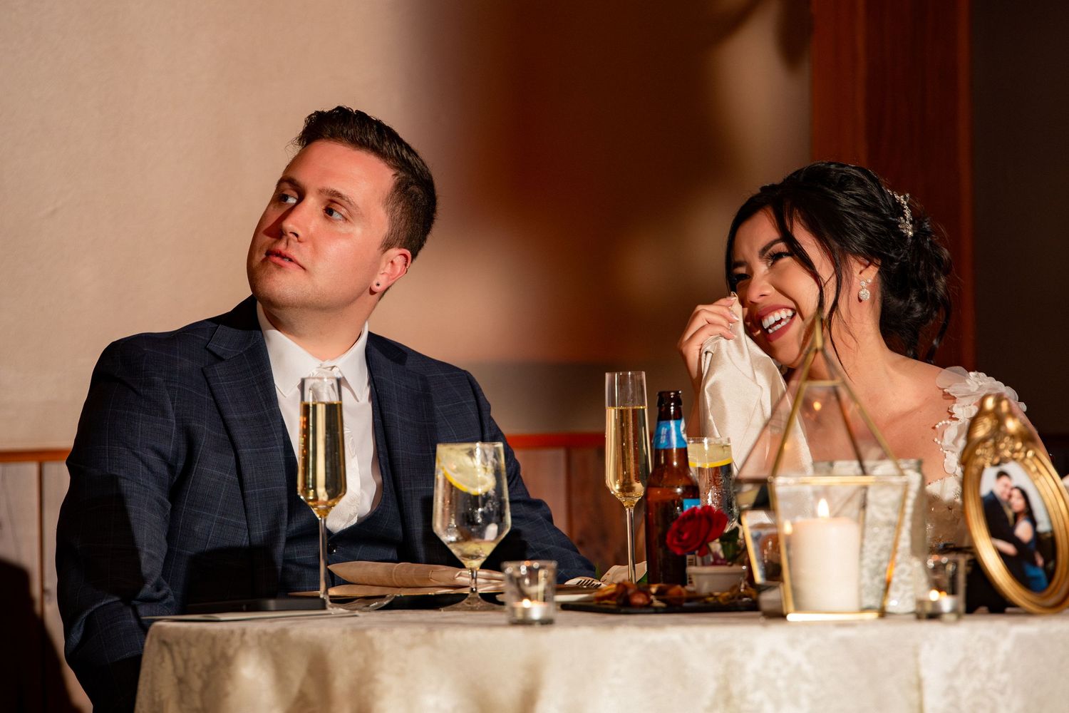 Bride wiping tears while groom smiles during heartfelt wedding reception speeches at their sweetheart table, Harrington Farm, Princeton, MA