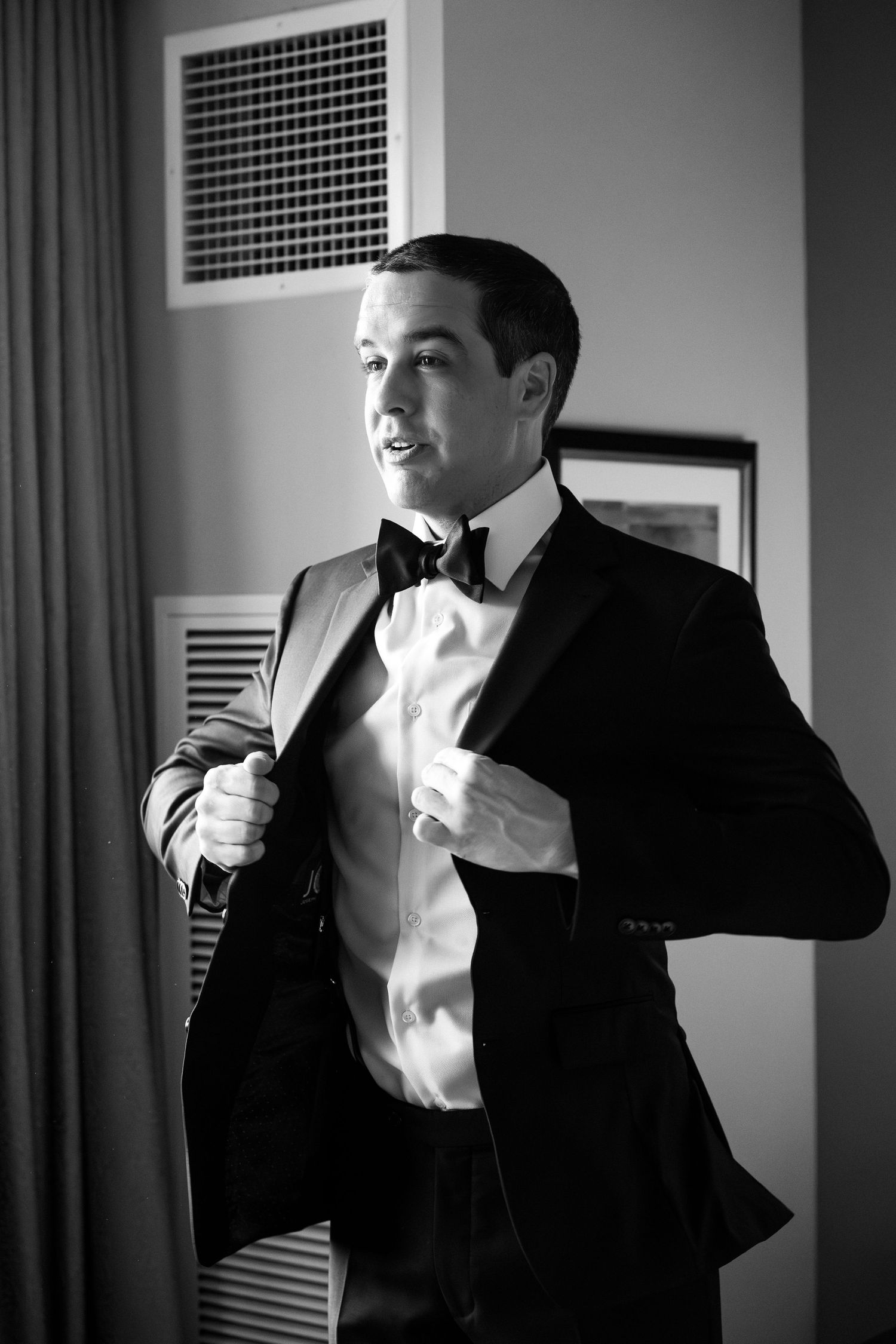 Dapper groom in black tuxedo adjusting jacket in black and white wedding portrait, Battery Wharf Hotel, Boston, MA