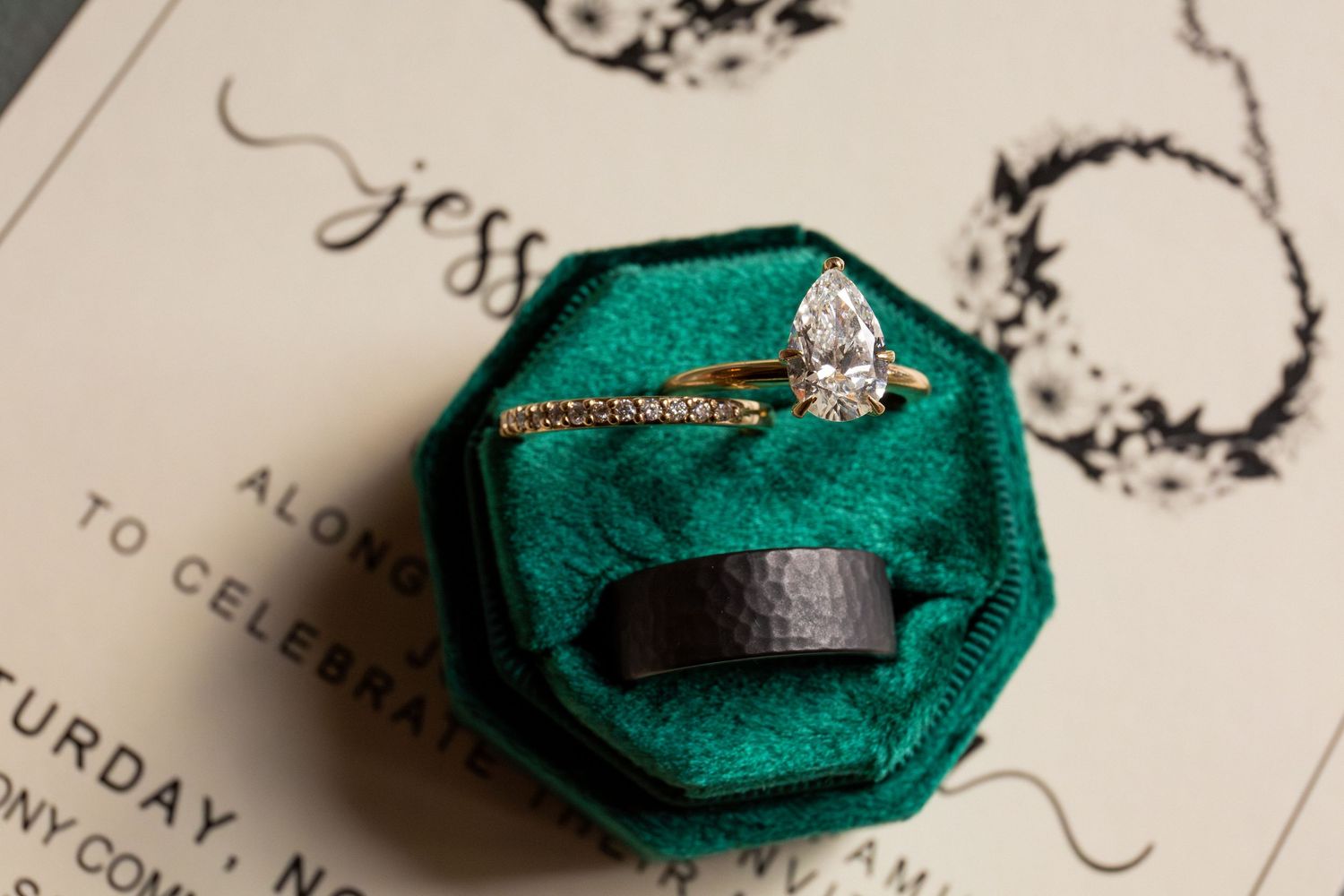 Pear-shaped diamond engagement ring and black wedding band displayed in green velvet ring box, Battery Wharf Hotel, Boston, MA