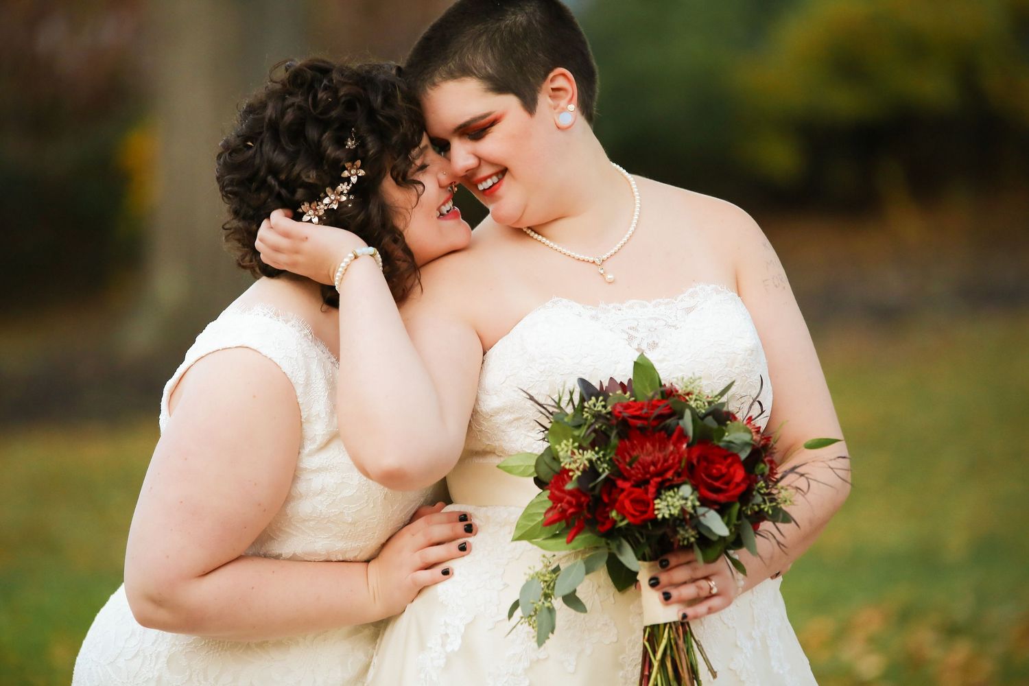 Two brides share a tender embrace holding red roses bouquet during outdoor autumn wedding, Inn on Boltwood, Amherst, MA