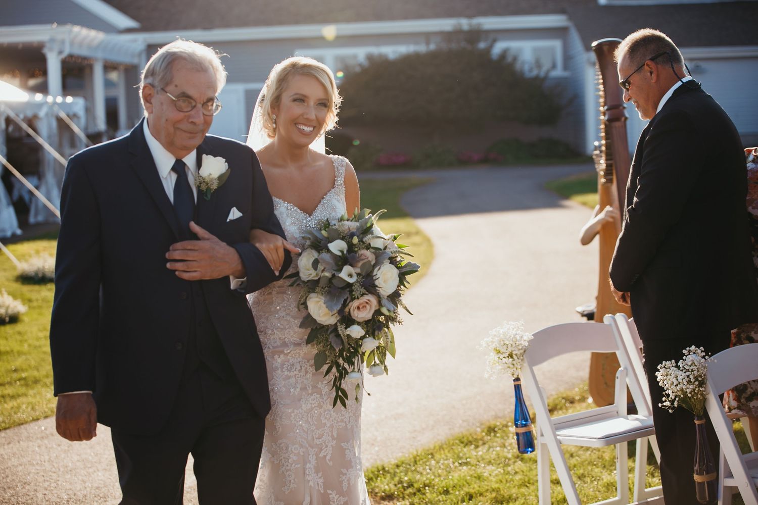 Smiling bride in lace gown holding a white bouquet, walking down the aisle with her father, White Cliffs Country Club, Plymouth, MA