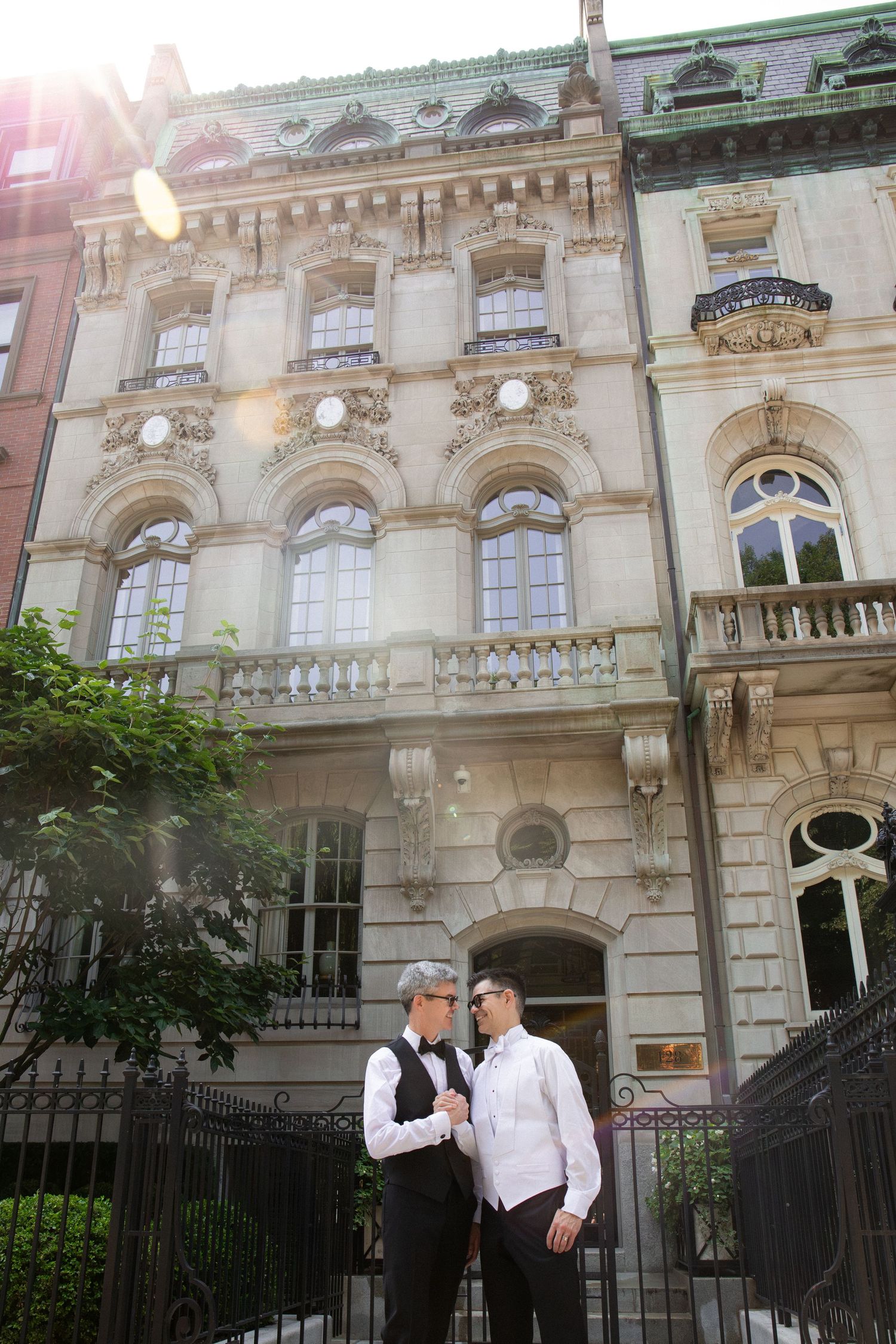 Two grooms in formal attire share a moment outside an ornate historic building on wedding day, Commonwealth Avenue Mall, Boston, MA