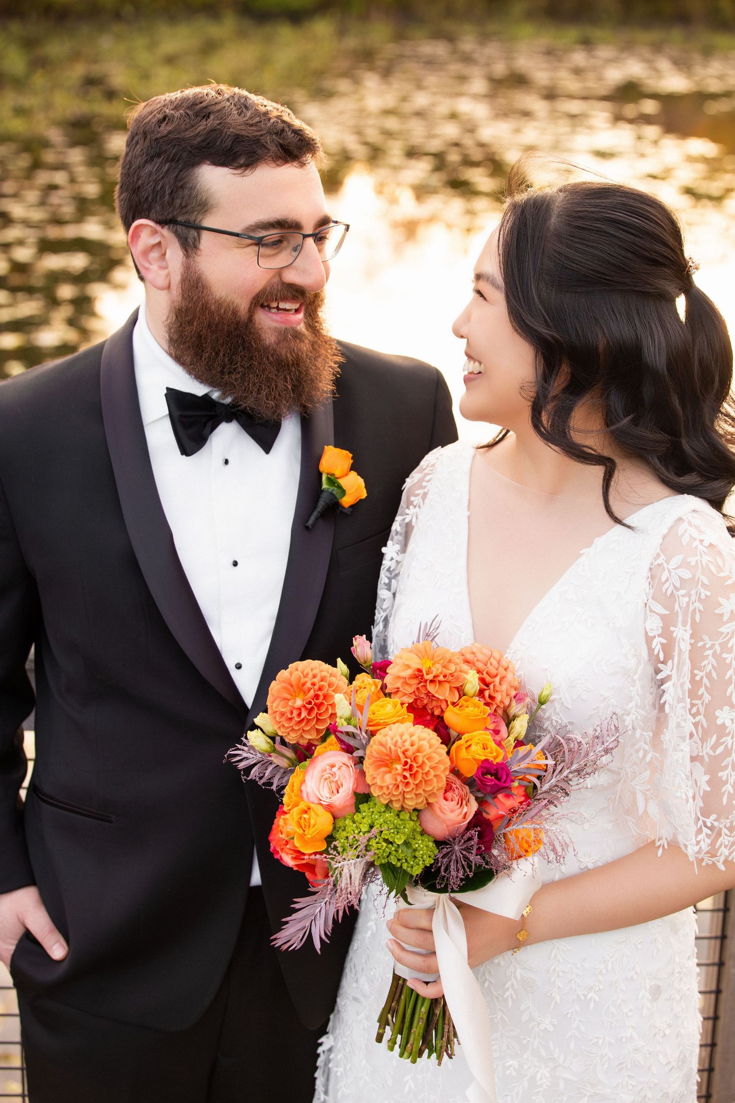 Smiling bride and groom share a joyful moment holding a colorful orange and pink bouquet, Alewife Brook Reservation, Cambridge, MA