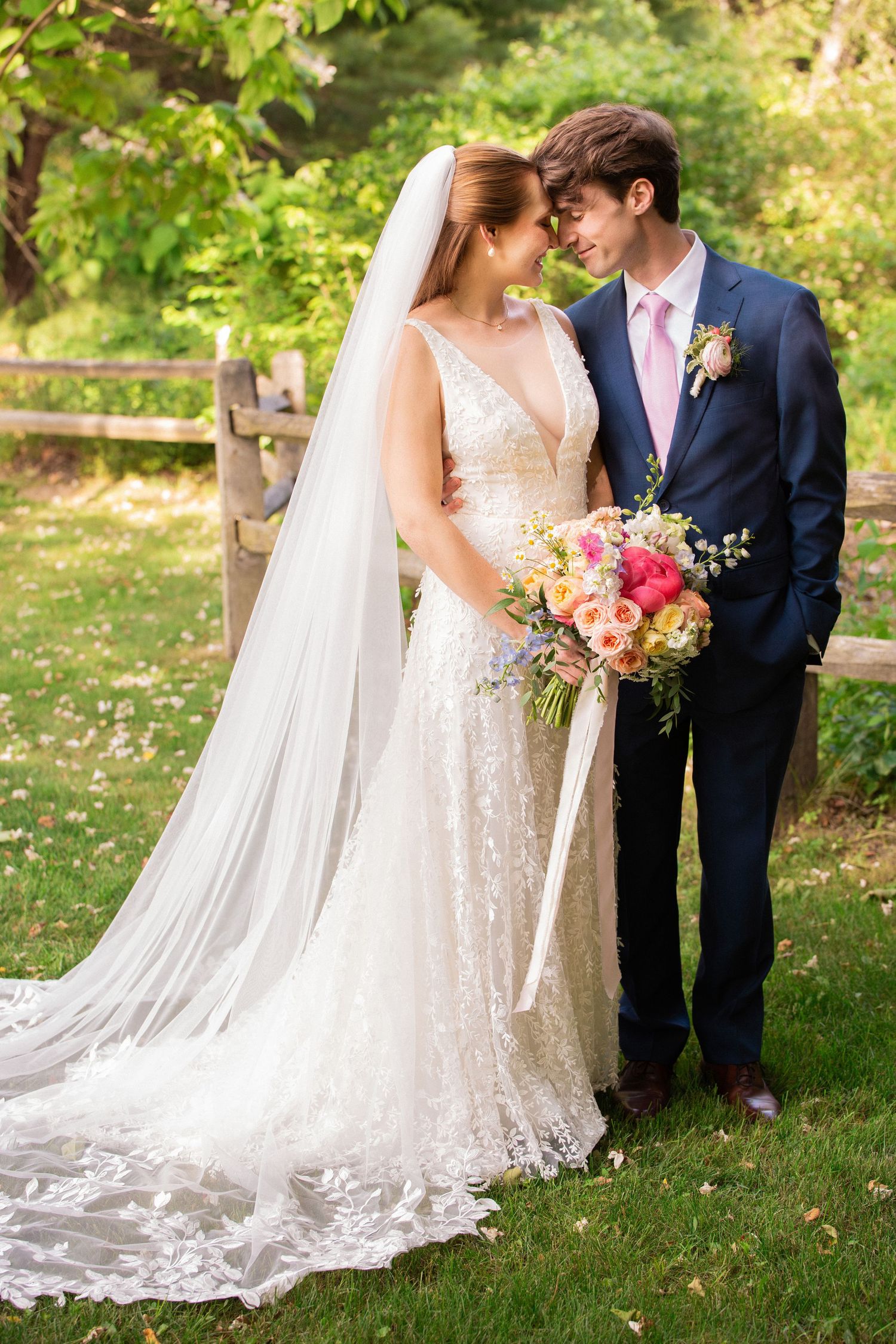 Bride in lace gown with long veil and groom in navy suit touching foreheads outdoors, Grove at Briar Barn Inn, Rowley, MA