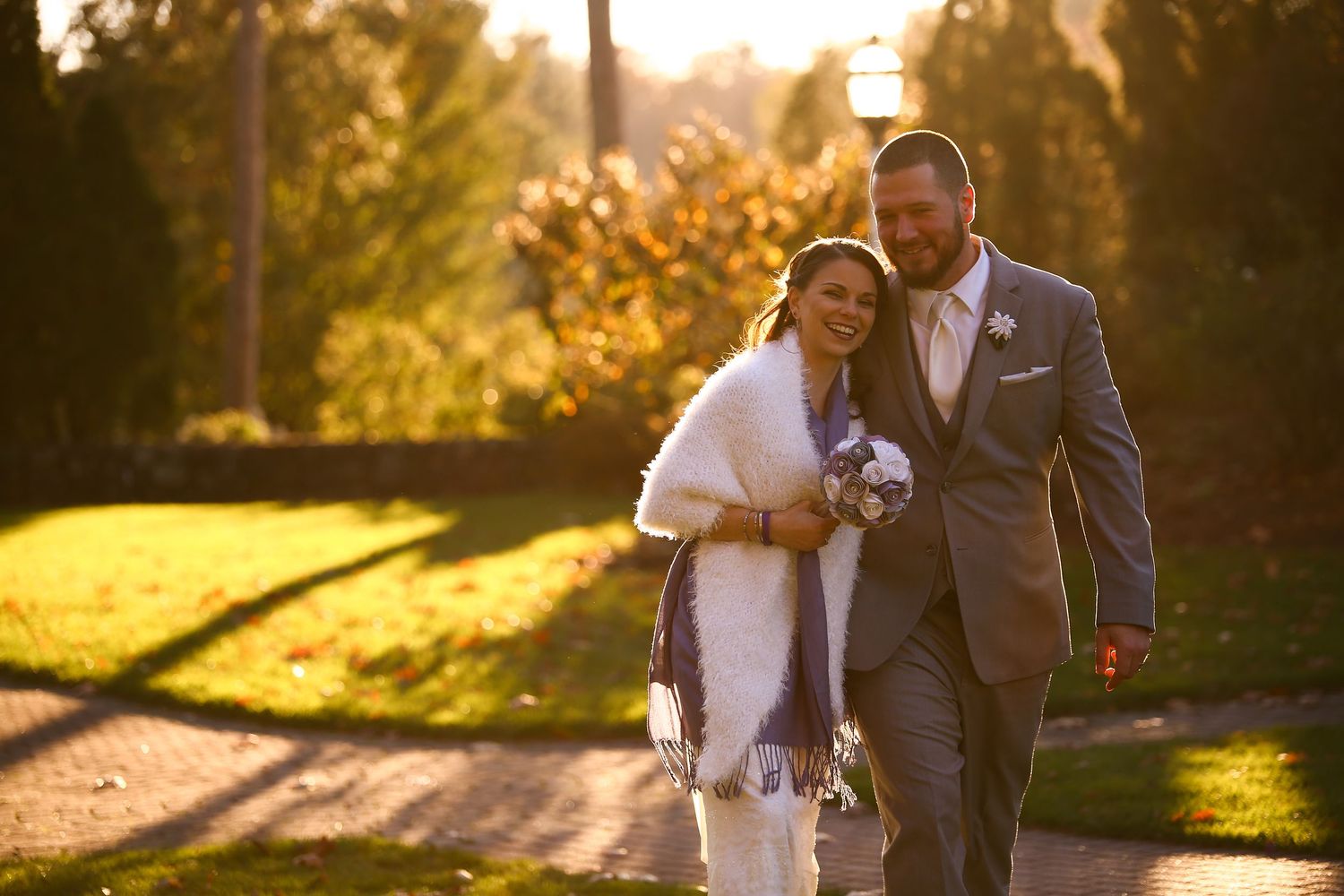 Happy bride and groom walk together at golden hour in autumn park, bride wrapped in white shawl, Xenia Helix Photography, Boston, MA