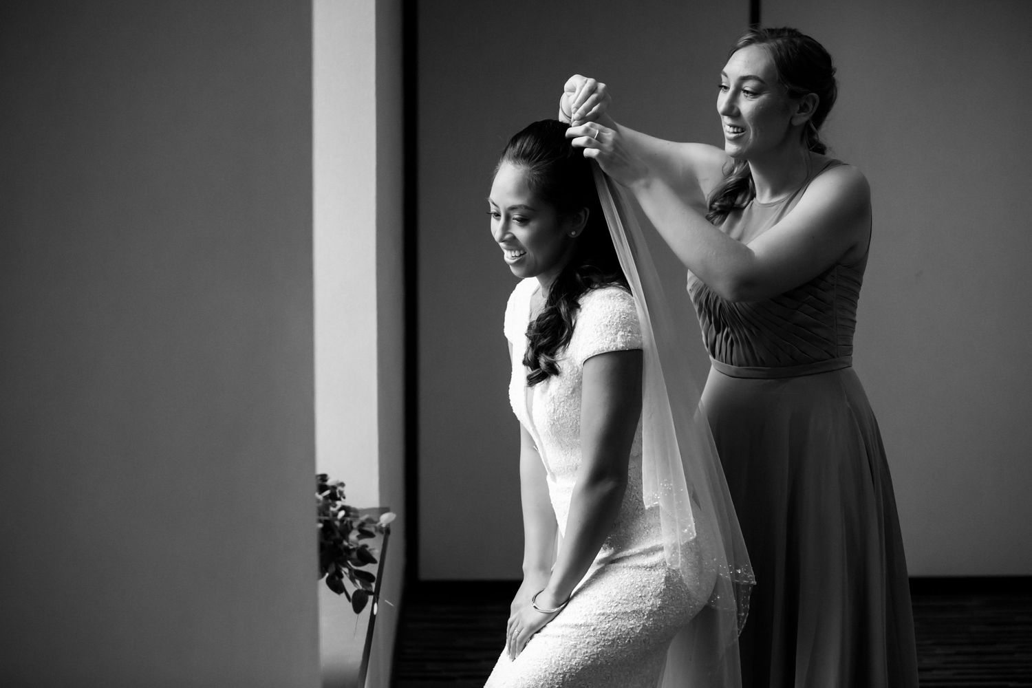 Black & white photo of bridesmaid carefully placing veil on smiling bride before wedding ceremony, Courtyard by Marriott Boston Downtown,