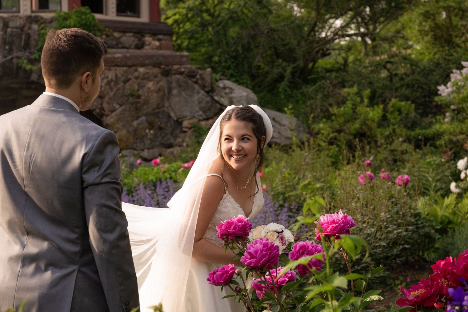 Smiling bride in  laced gown and veil walking with the groom through a vibrant garden with pink peonies, Estate at Moraine Farm, Beverly, MA