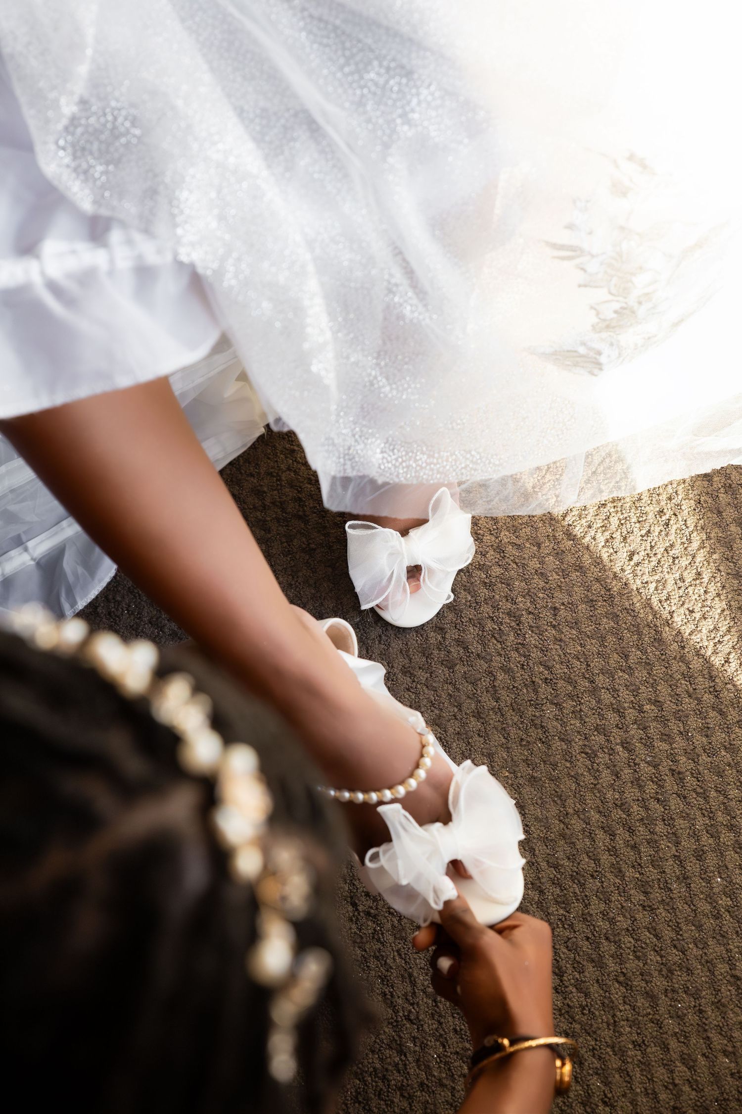 Bridesmaid fastening white bow shoes with pearl ankle straps on a bride in a white lace wedding gown, Independence Harbor, Assonet, MA