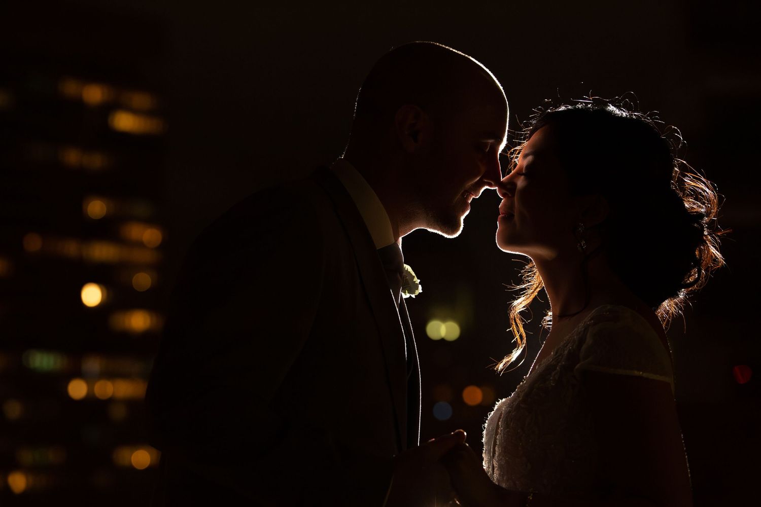 Romantic silhouette of a couple nearly kissing against a glowing city skyline at night on a rooftop, The Colonnade Hotel, Boston, MA