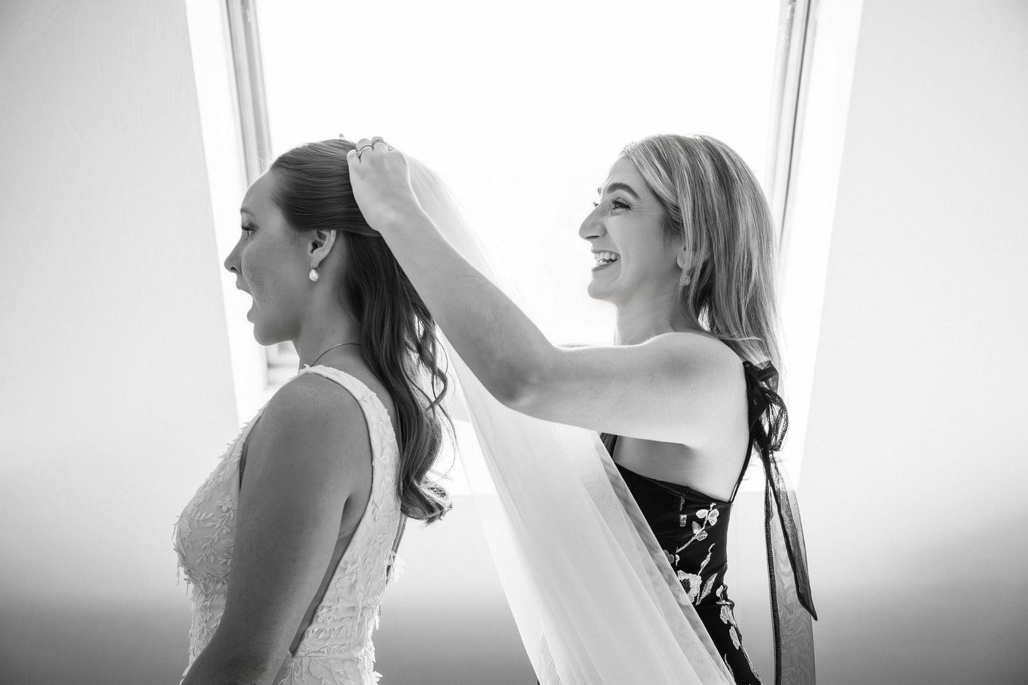 Bridesmaid helping bride adjust her veil in front of bright window in a black-and-white photo, Grove at Briar Barn Inn, Rowley, MA