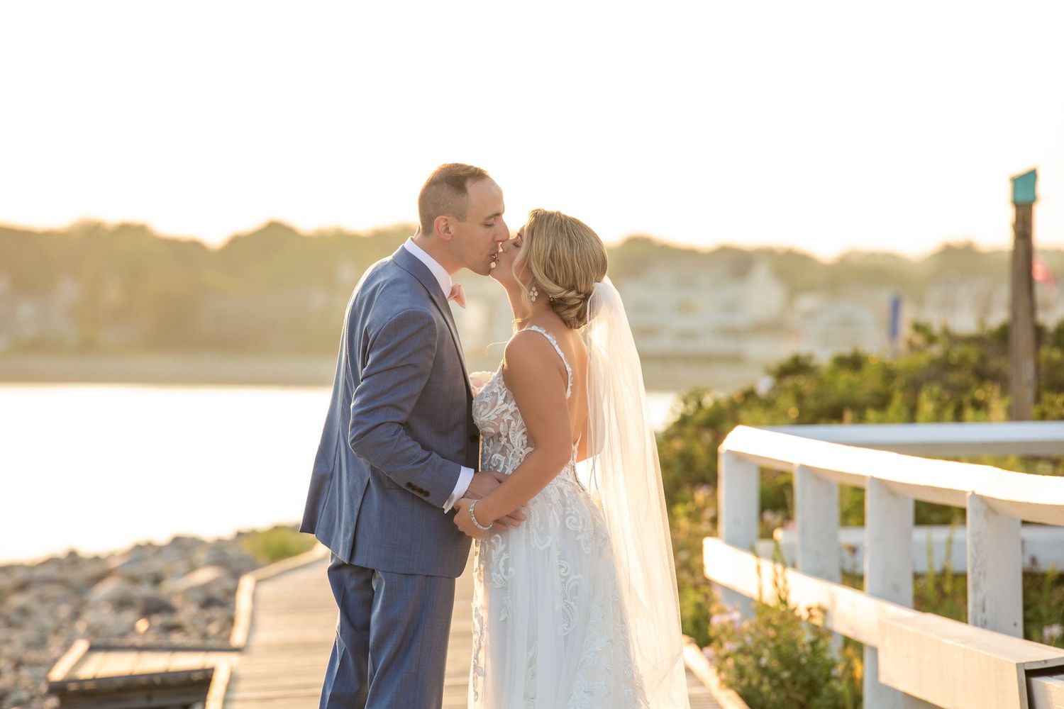 Bride and groom share a kiss on a waterfront boardwalk during golden hour, Scituate Lighthouse, Scituate, MA