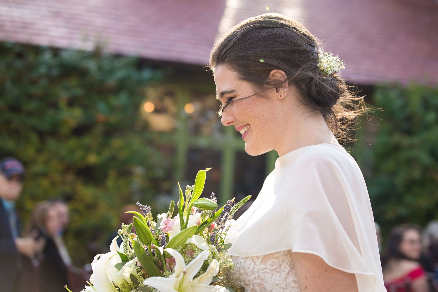Smiling bride in a white gown walks with a bouquet of white lilies, Willowdale Estate, Topsfield, MA