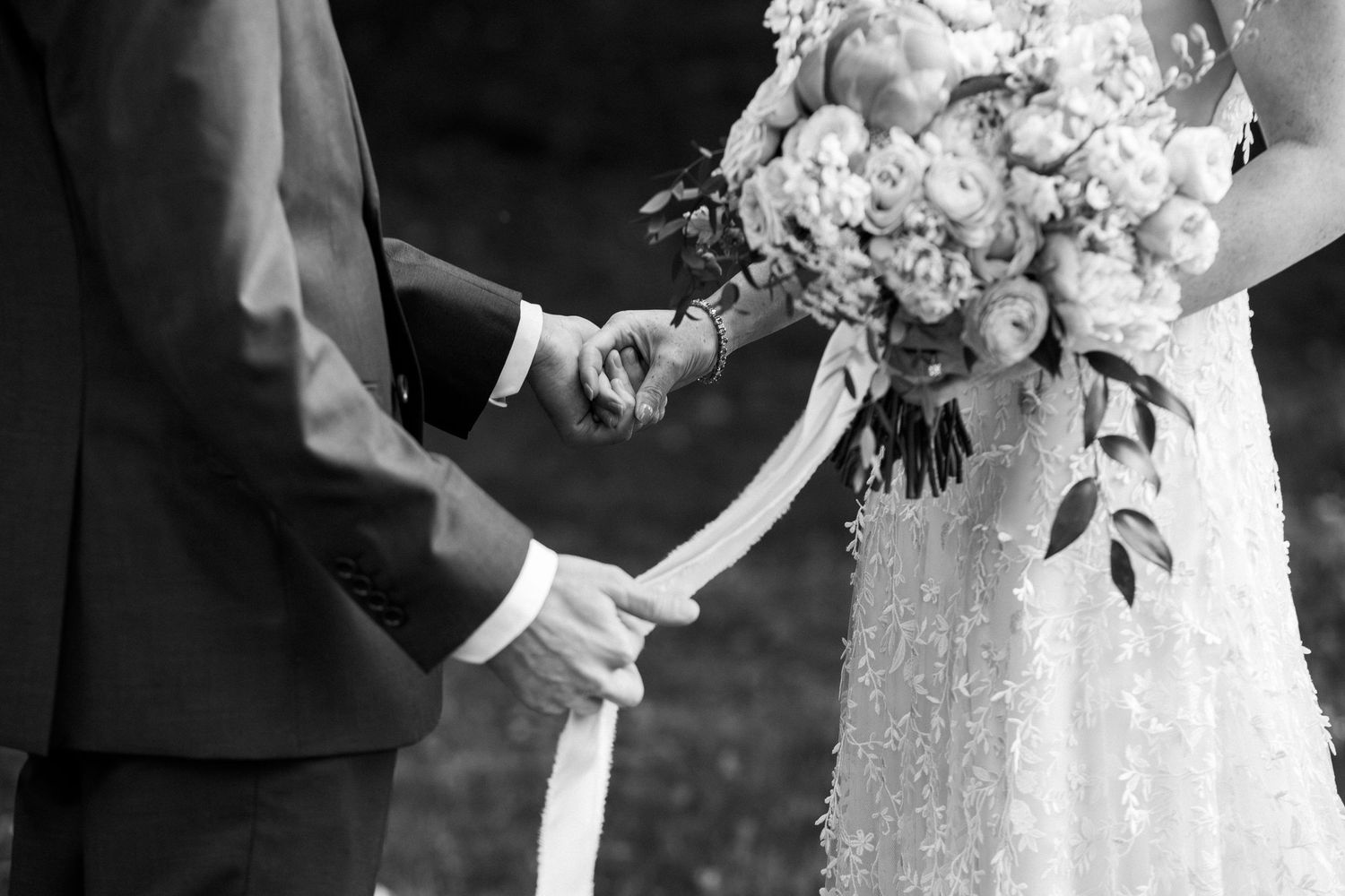 Black and white close-up of bride and groom holding hands with a lush floral bouquet during first look, Grove at Briar Barn Inn, Rowley, MA