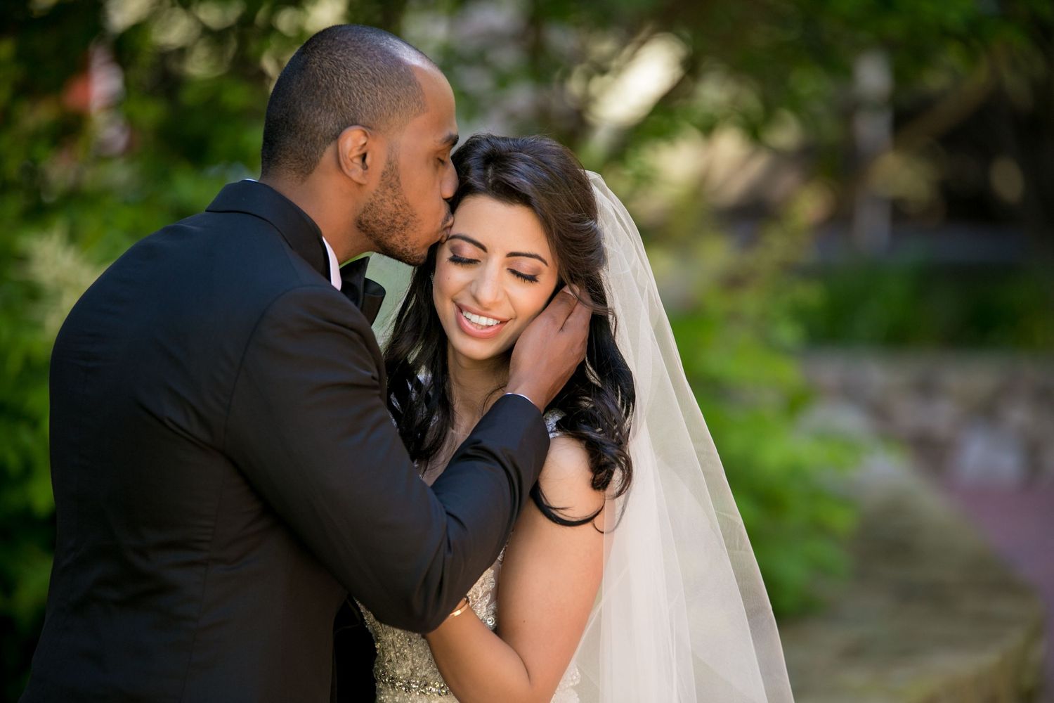 Groom tenderly kissing smiling bride on the cheek during outdoor wedding portrait, Mandarin Oriental Boston, MA