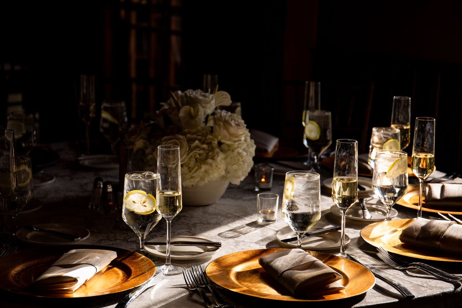 Wedding reception table set with gold chargers, champagne flutes, and white floral centerpiece in sunlight, Harrington Farm, Princeton, MA