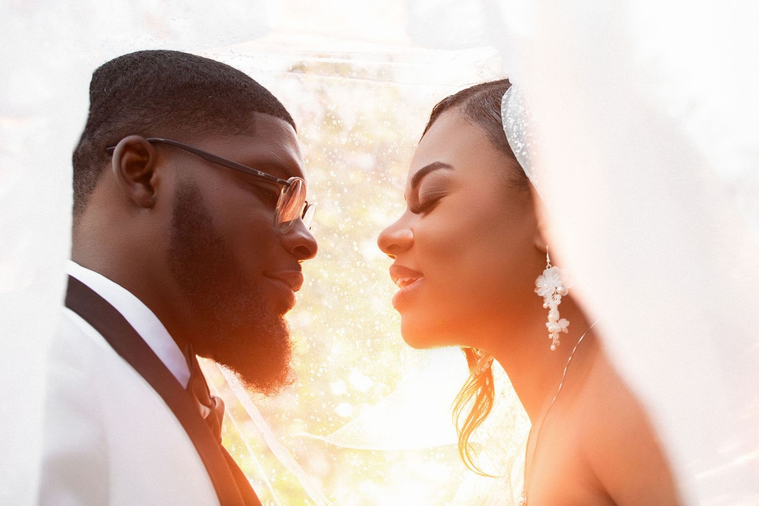 Bride and groom sharing an intimate moment under a veil in warm golden sunlight, Independence Harbor, Assonet, MA