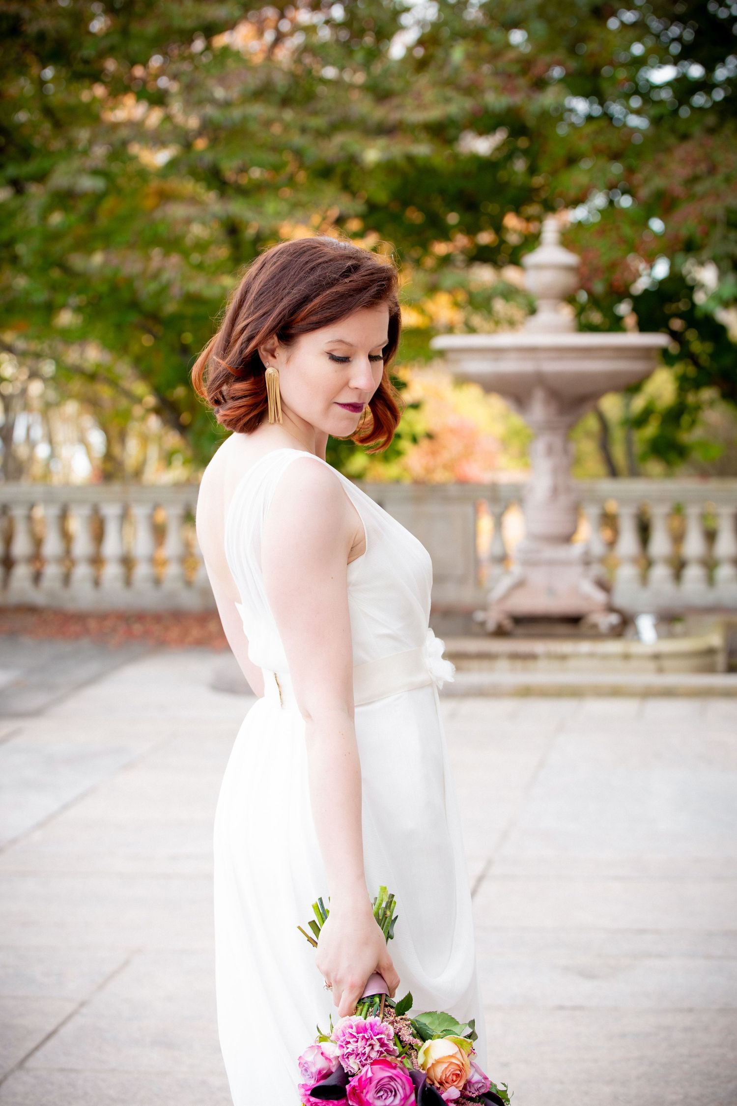 Elegant bride in white gown holding colorful bouquet beside stone fountain in autumn garden, 	Robbins Memorial Town Hall, Arlington, MA